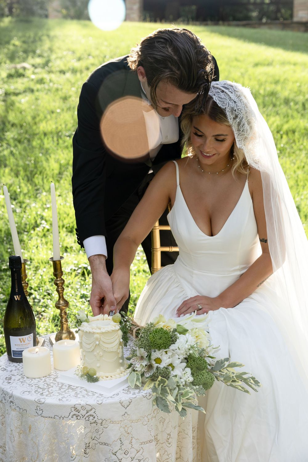 Bride in white wedding dress signs marriage certificate during outdoor ceremony with greenery in background.