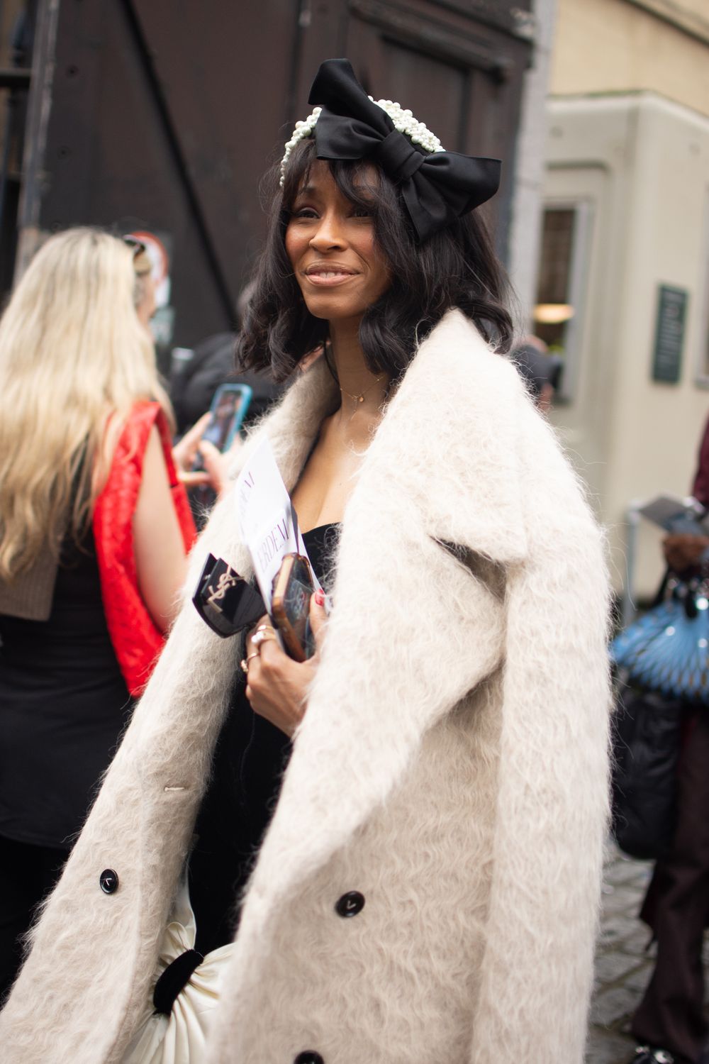 A street style fashion photo of a woman wearing a plush white coat and a black hat worn at the ERDEM fashion show at the British Museum
