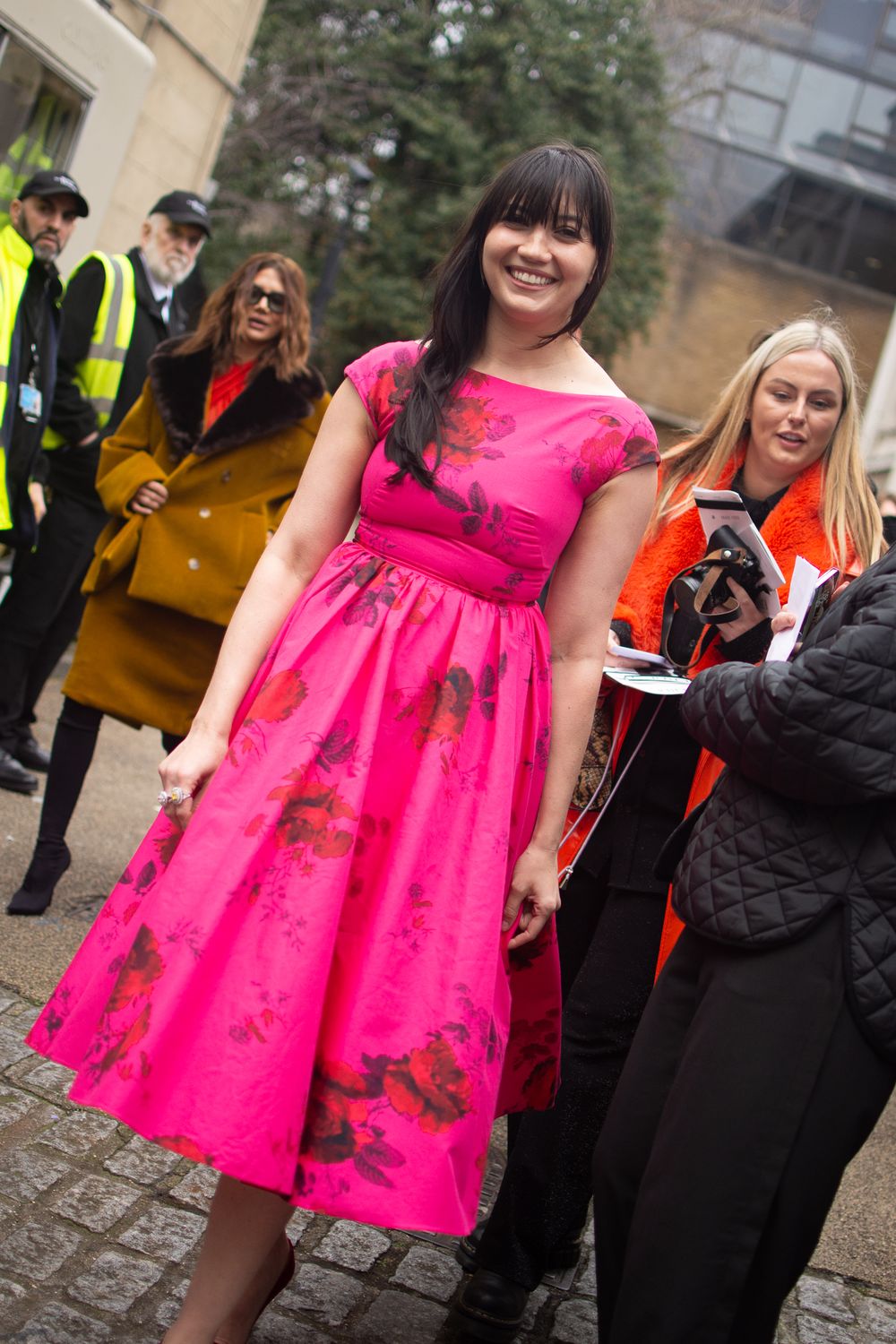 A woman wearing a bright pink ERDEM dress at an outdoor gathering with other guests nearby in London