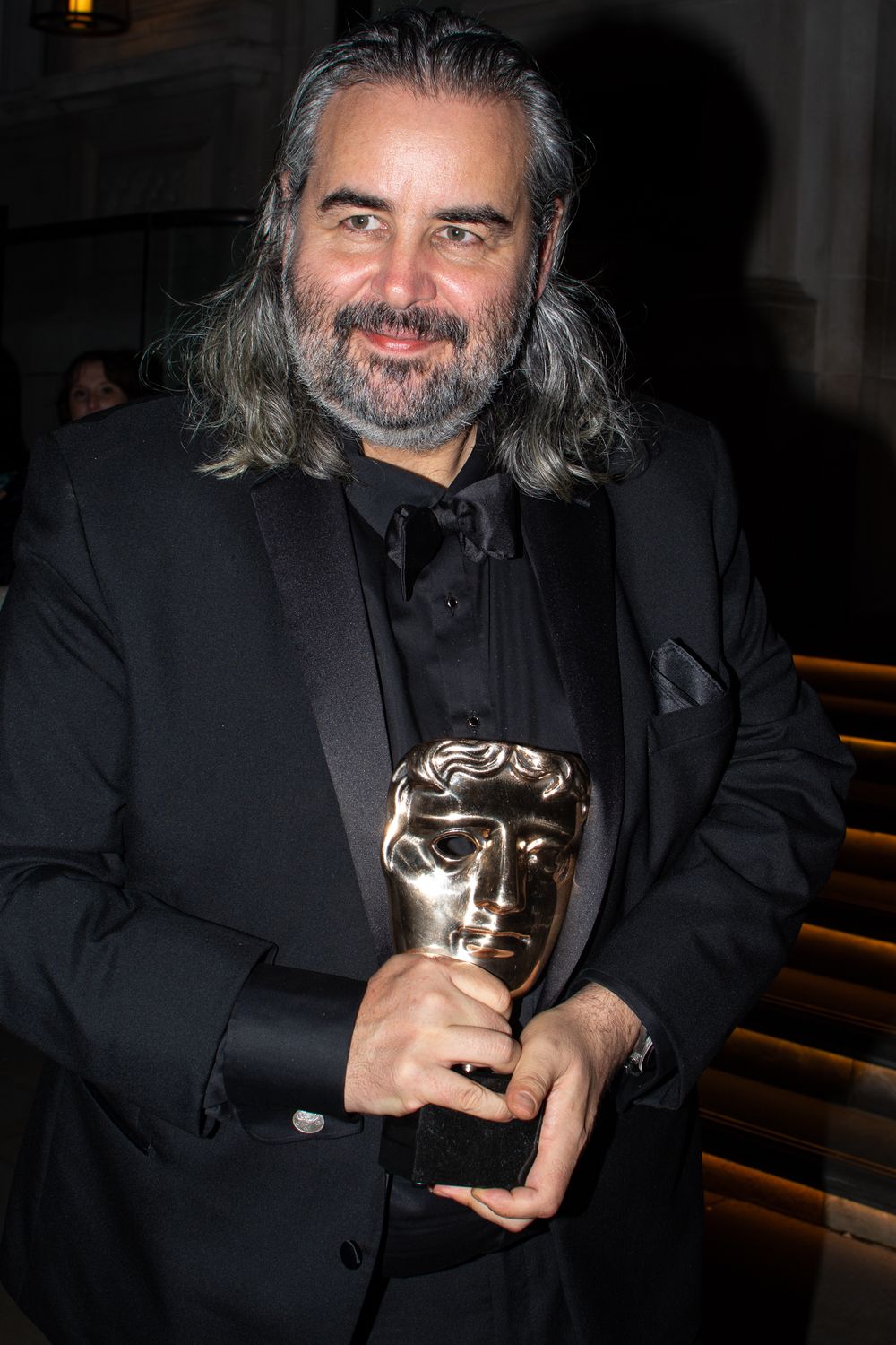 Hoyte van Hoytema in black suit holding a BAFTA award trophy at an evening event in London
