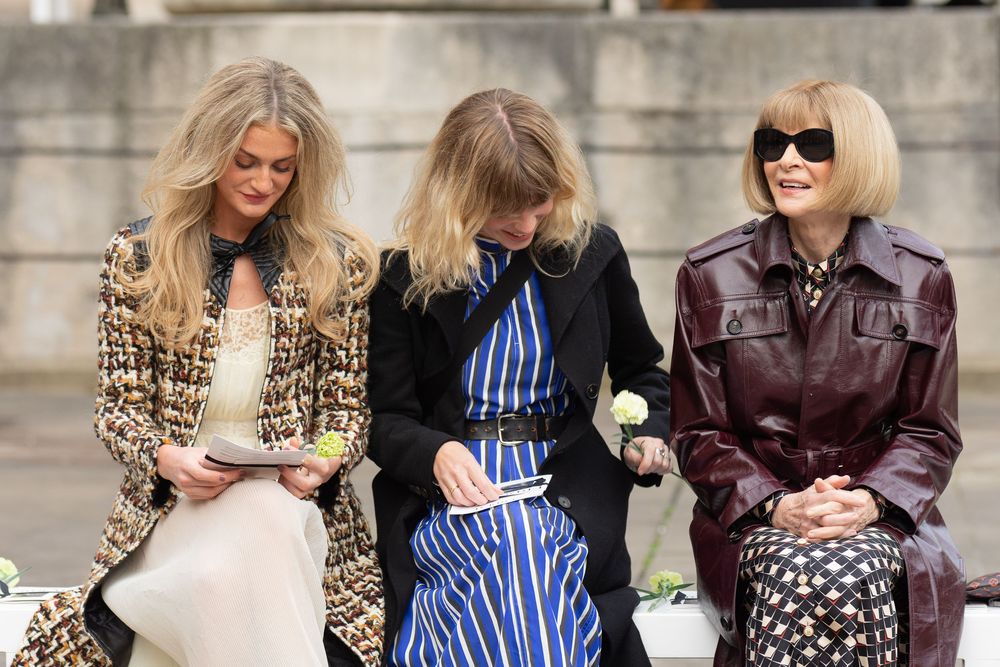 Anna Wintour and 2 women sit together at a fashion event, wearing chic outfits including leopard print, blue stripes, and burgundy leather.