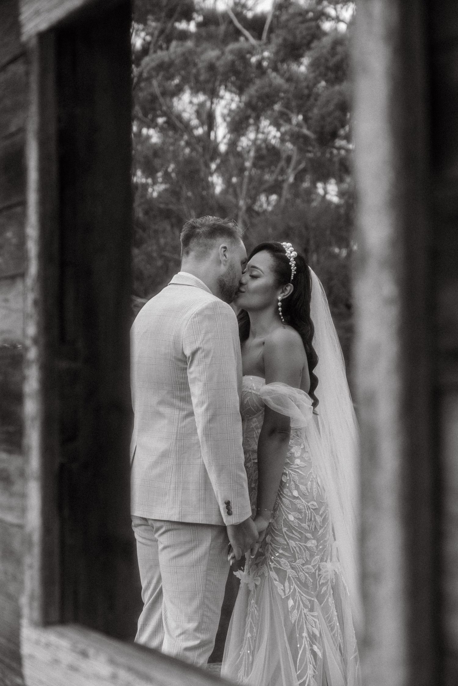 Romantic outdoor romance scene showing newlyweds in white attire embracing near rustic stone wall with elegant decor.