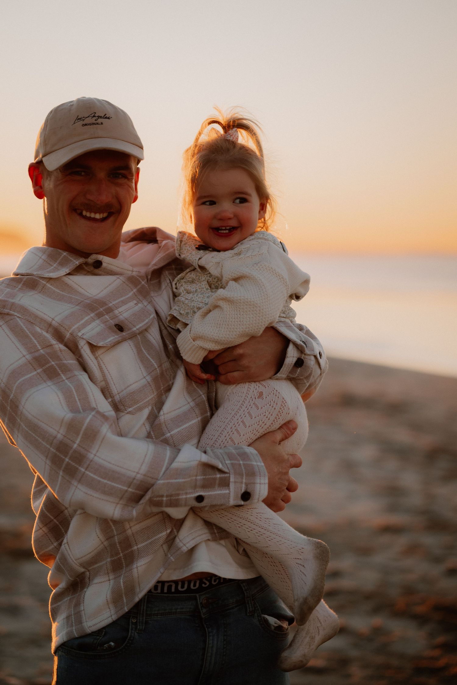 Candid sunset portraits capture joyful laughter and bonding moments between loved ones on a scenic beach.