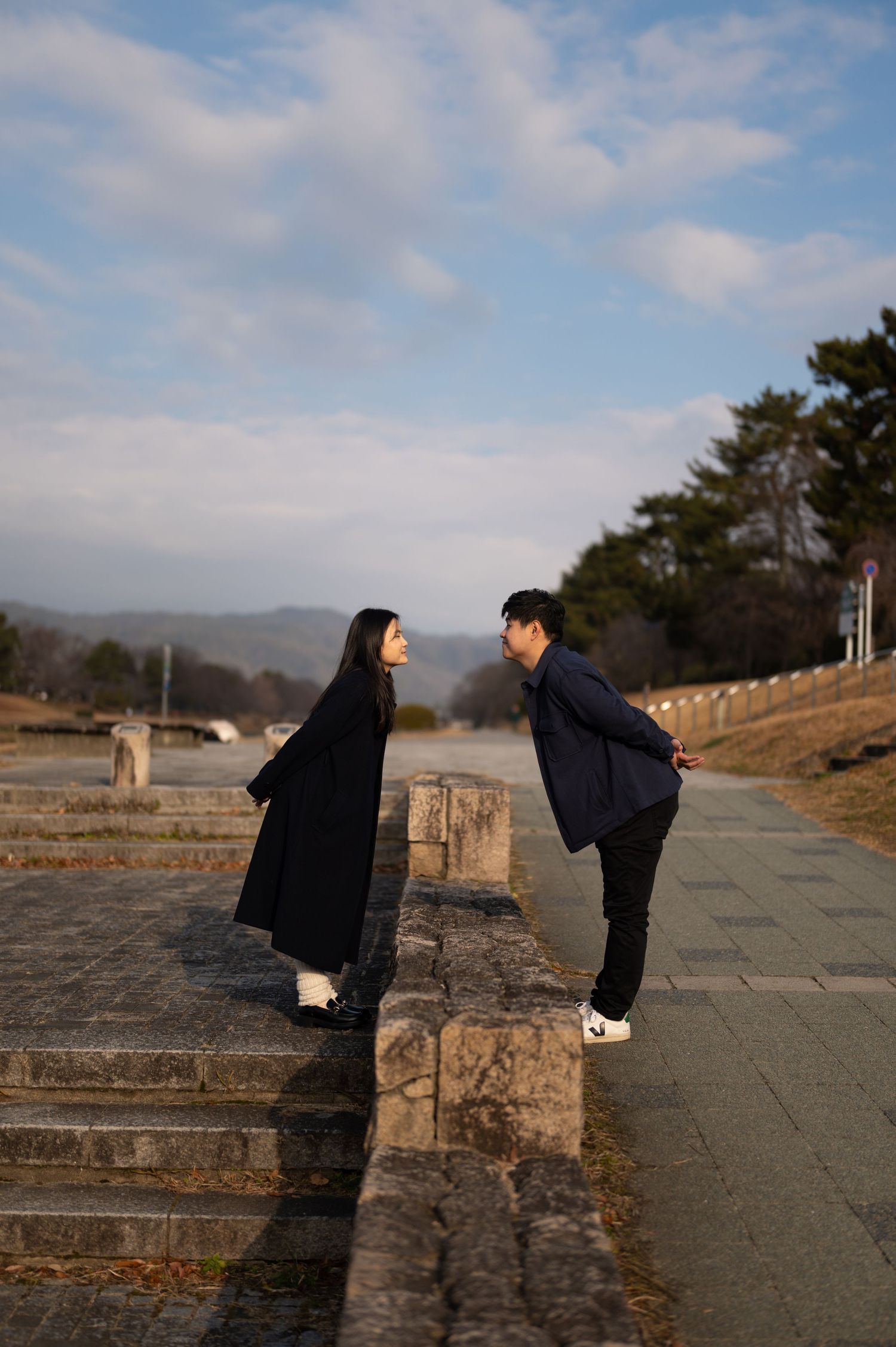 Couple facing each other on stone steps at a historic outdoor site with blue sky and trees.