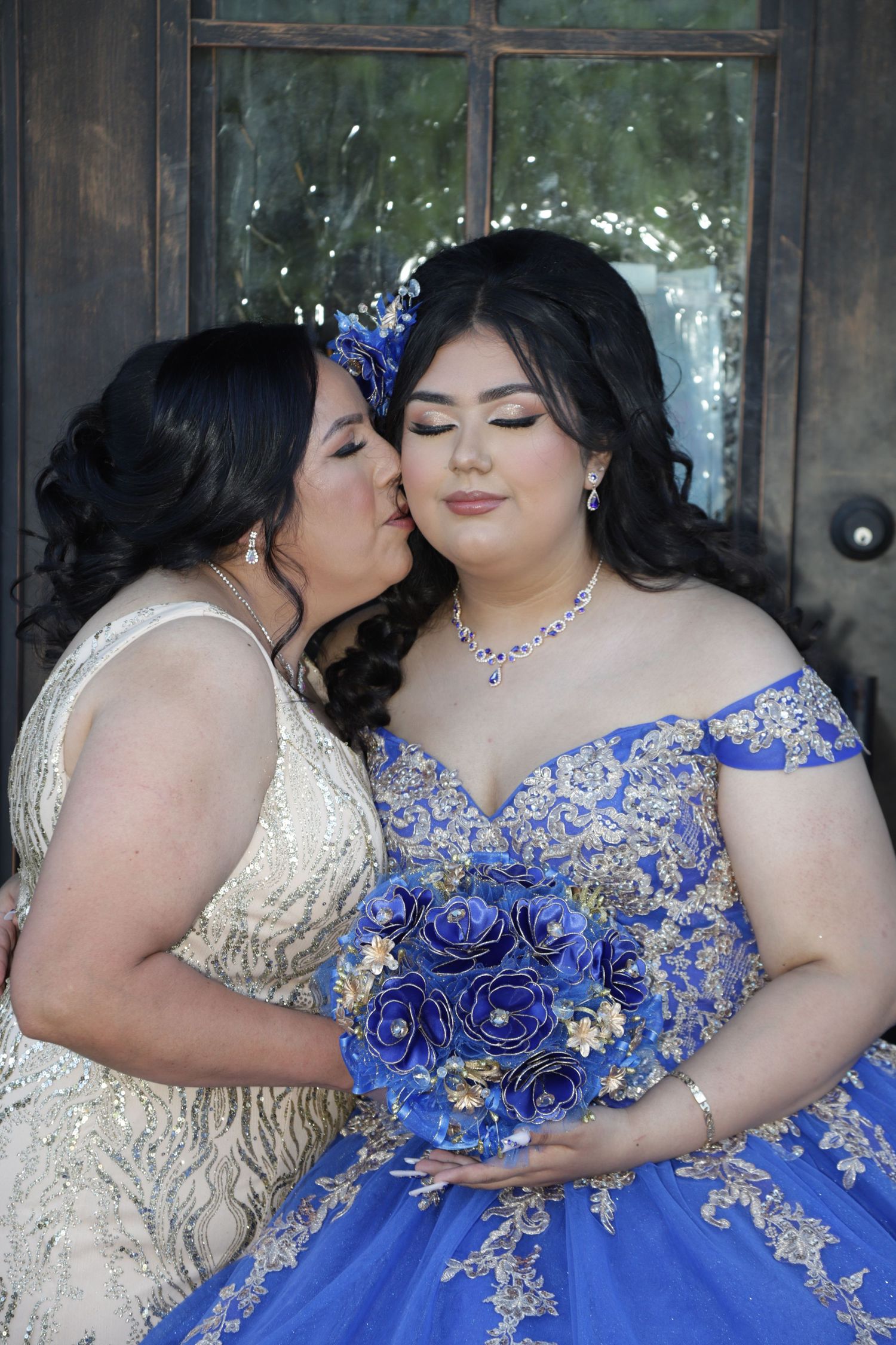 Bridesmaids in cream dresses pose with someone in a royal blue gown adorned with sparkly details and holding blue roses.