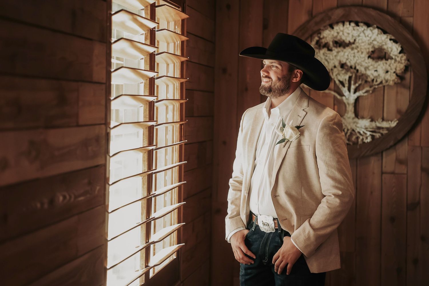 Groom adjusting blazer by rustic barn window at Whispering Oaks