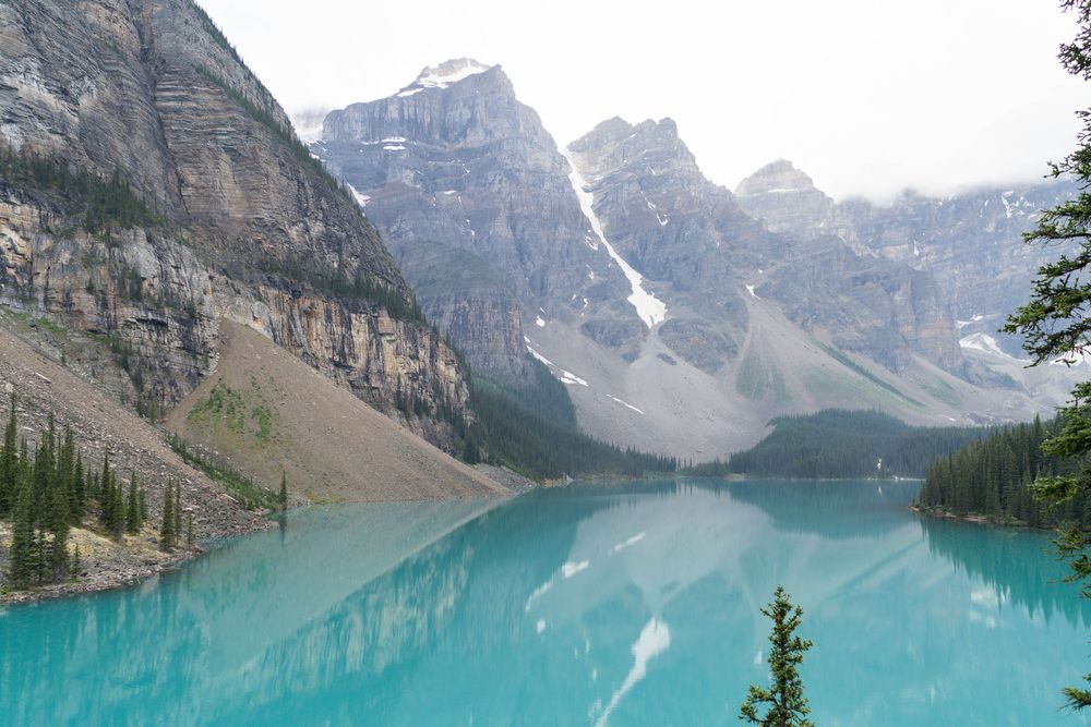 Panoramic view of Moraine Lake's pristine turquoise waters surrounded by snow-capped peaks in the Canadian Rockies.