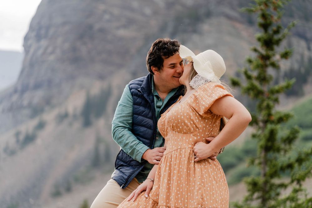 A couple shares a romantic moment against a backdrop of majestic mountains and a turquoise lake.