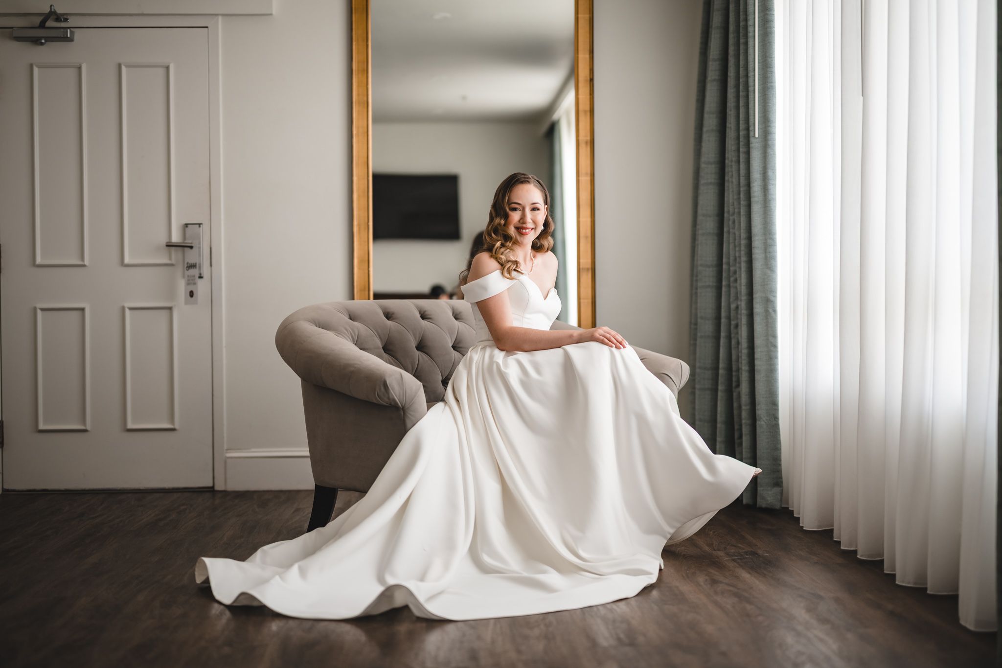 An elegant off-shoulder wedding dress photographed in a minimalist room setting.