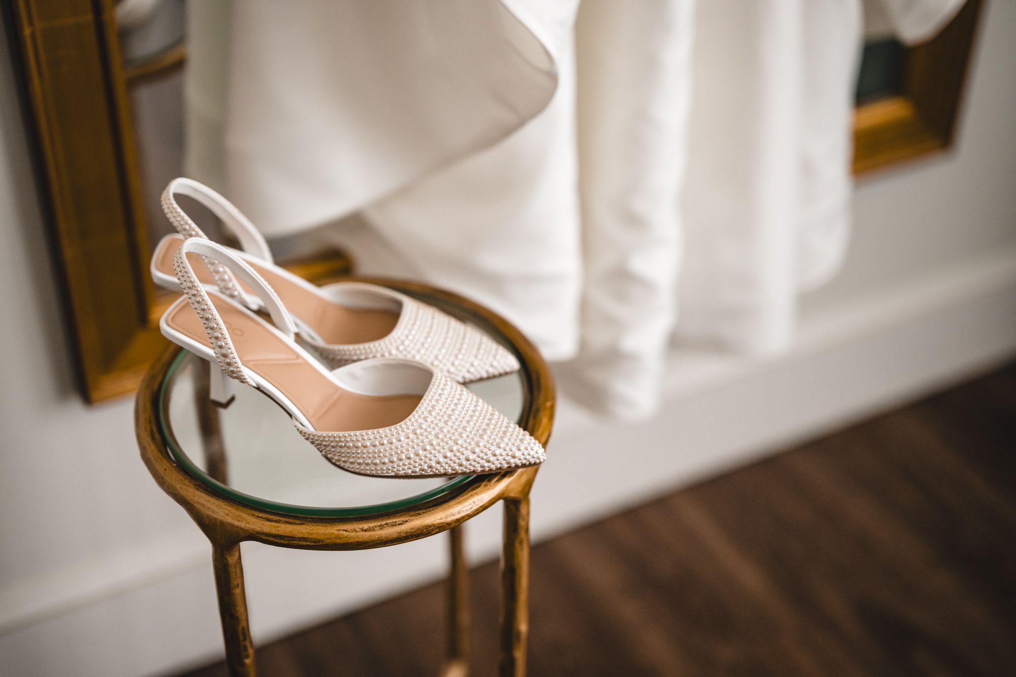 Wedding accessories including blush heels, floral bouquet, and invitation details arranged on white surface.