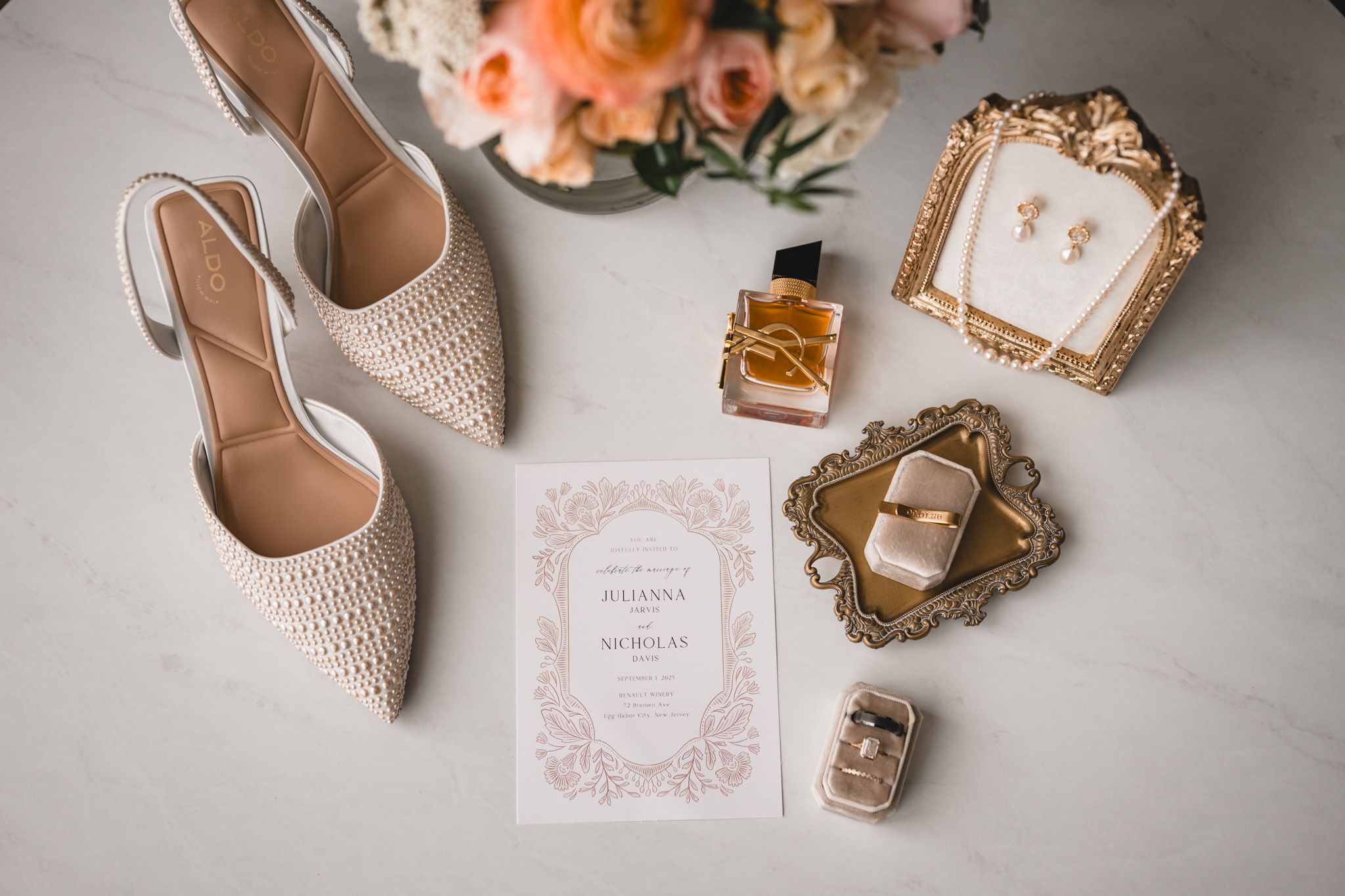 Delicate wedding details featuring rings in velvet box, invitations, and perfume bottle.