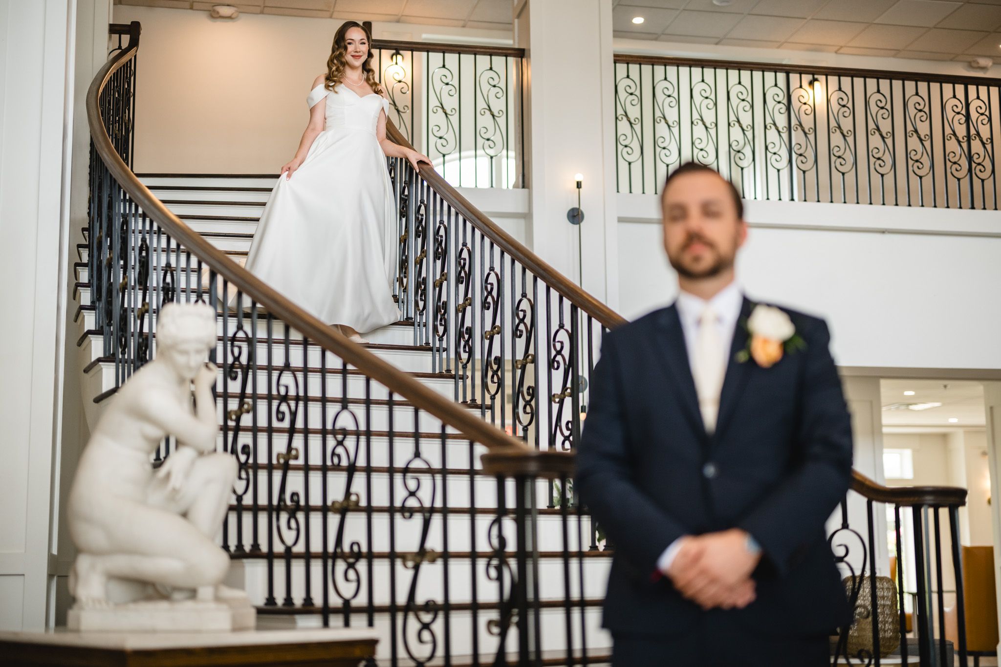 First look wedding moment captured on elegant staircase with ornate iron railings.