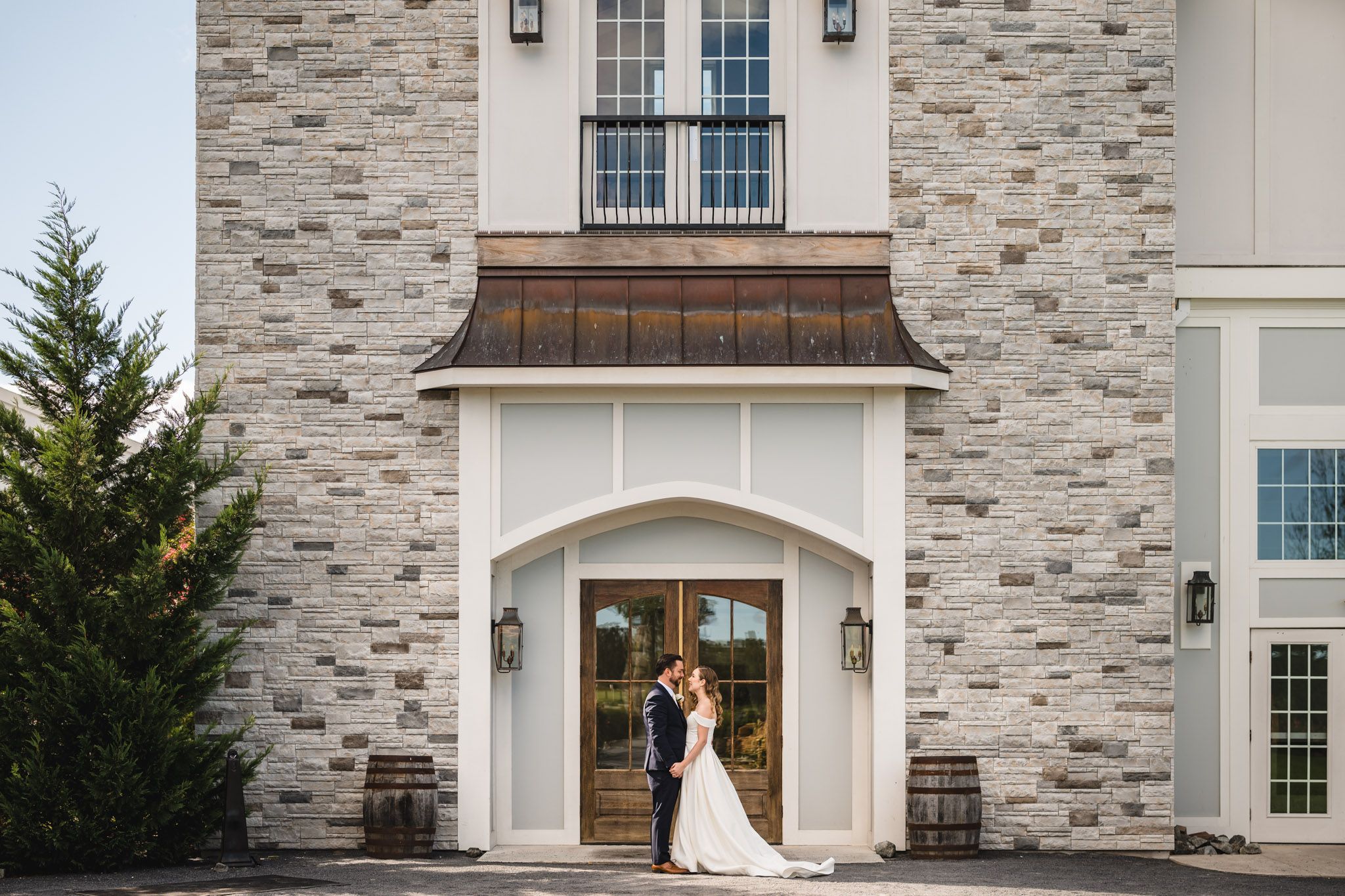 A wedding couple stands in the doorway of an elegant stone building with white trim.