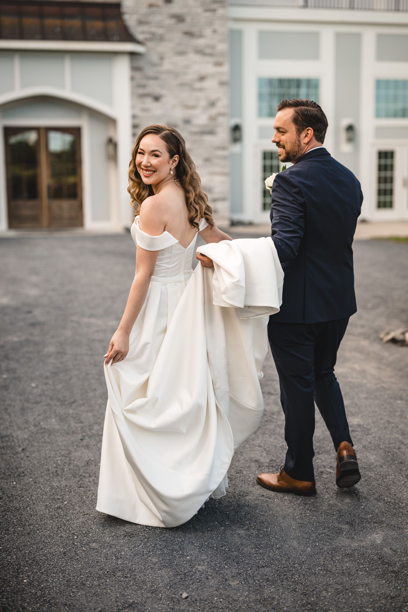 A couple in wedding attire shares a playful moment outside a stone building.