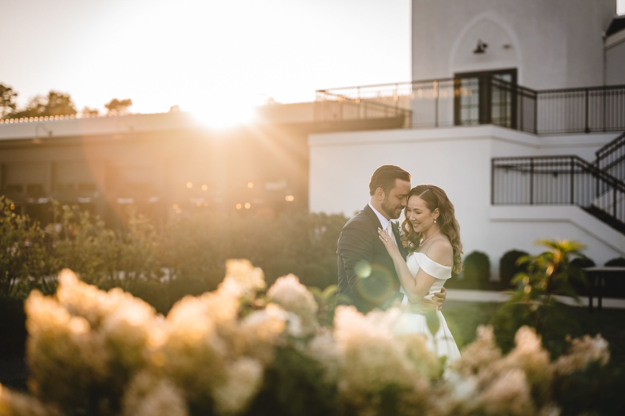 A couple embraces during golden hour with a white building in the background.