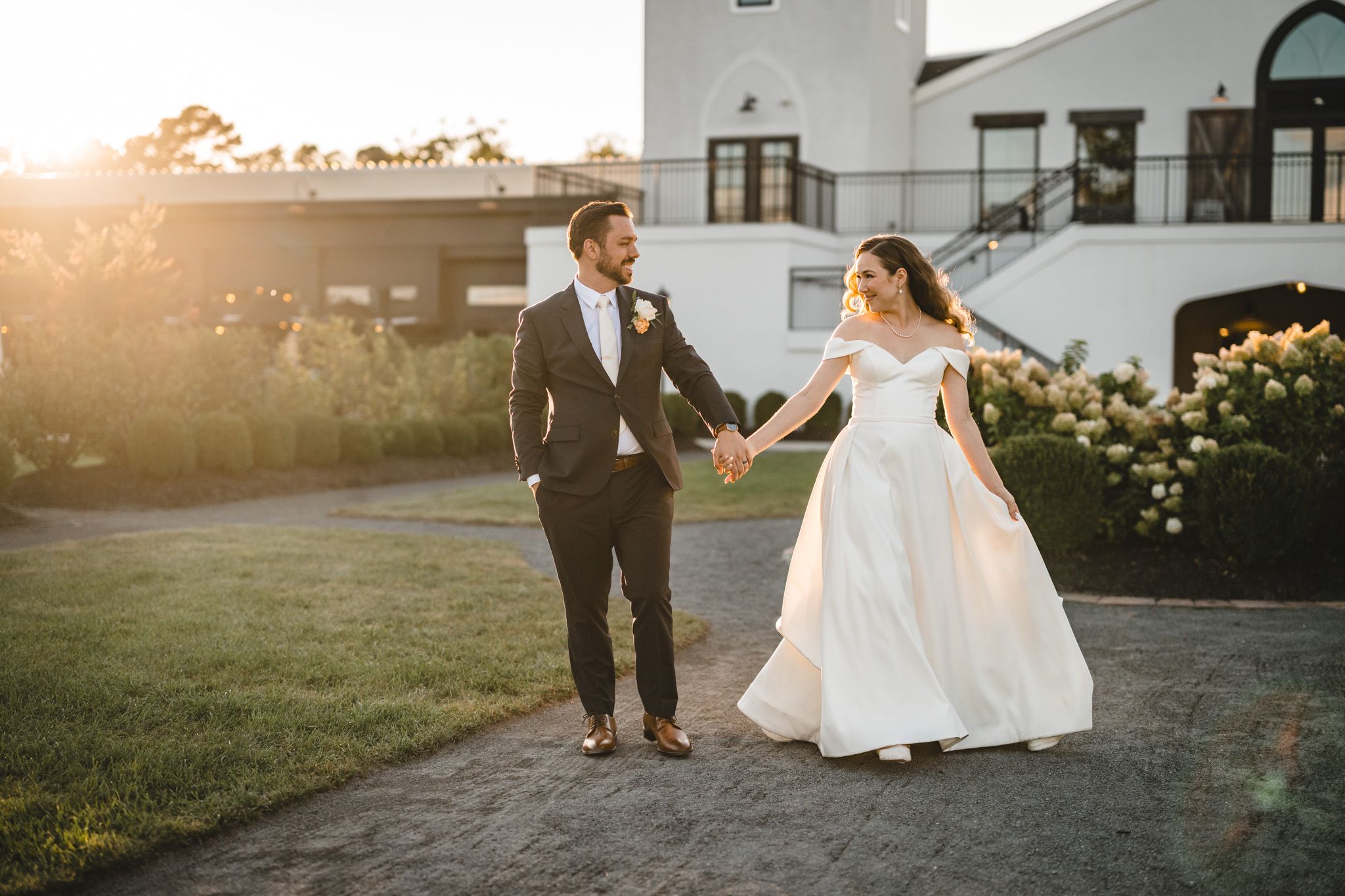 A couple walks hand in hand during sunset on their wedding day.