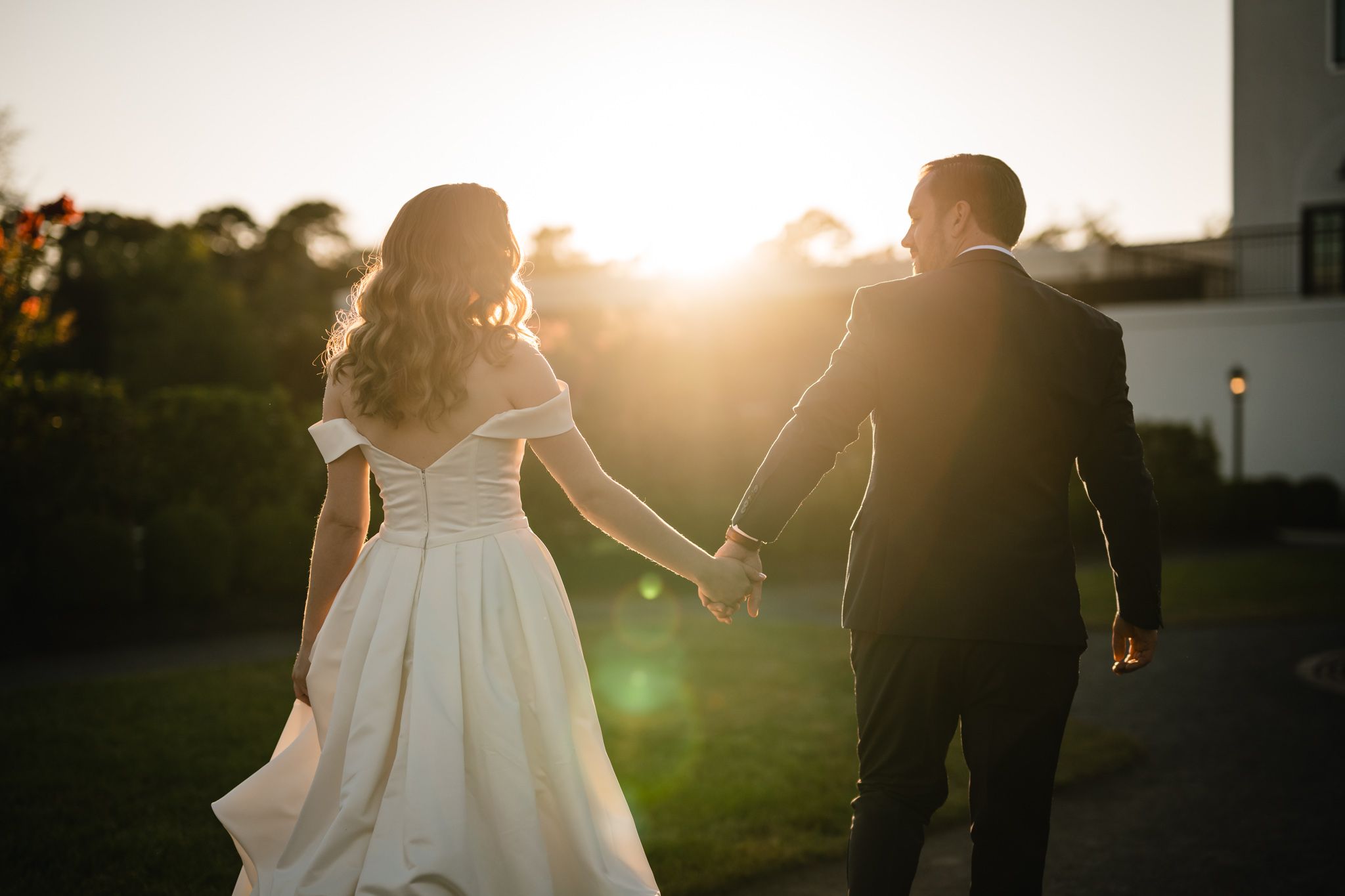 A couple walks hand in hand during golden hour with lens flare in the background.