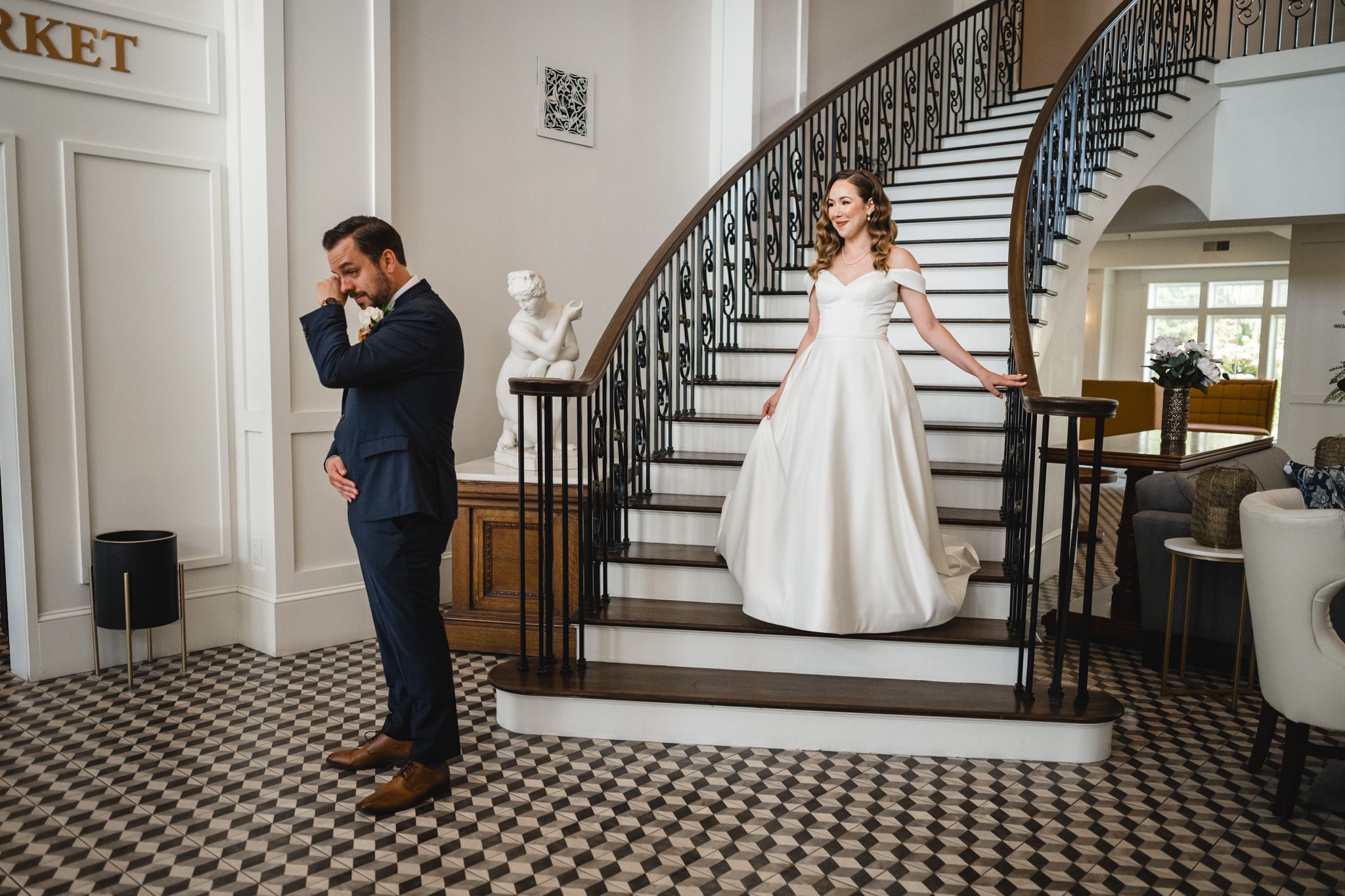 Couple shares emotional first look moment in grand venue with sweeping staircase.