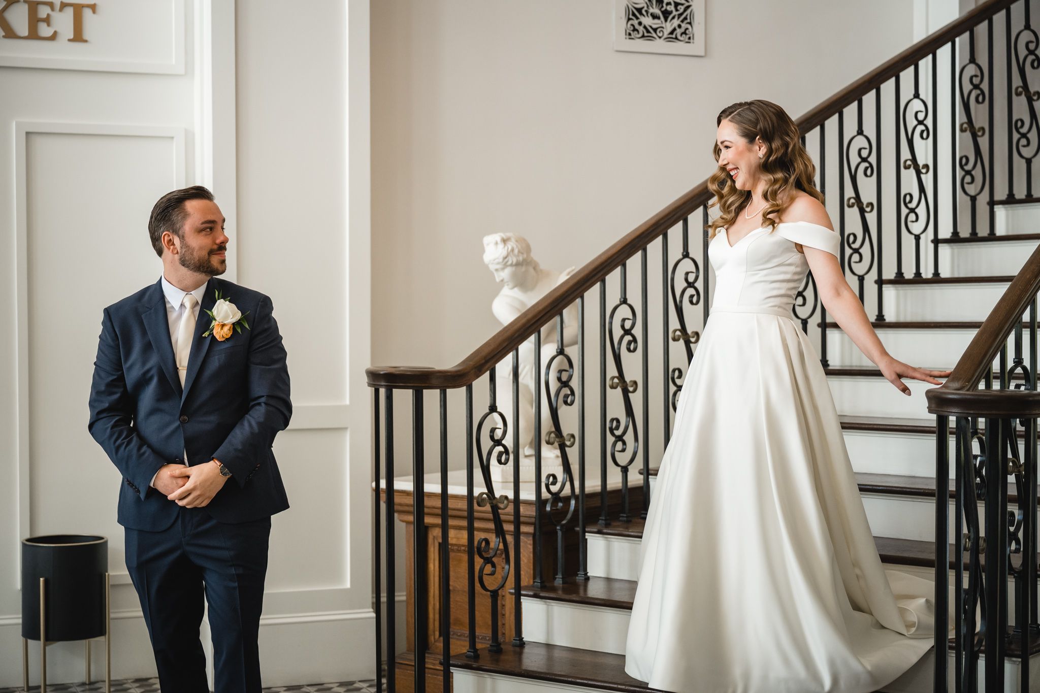 Bride and groom share joyful reactions during first look in elegant white interior.