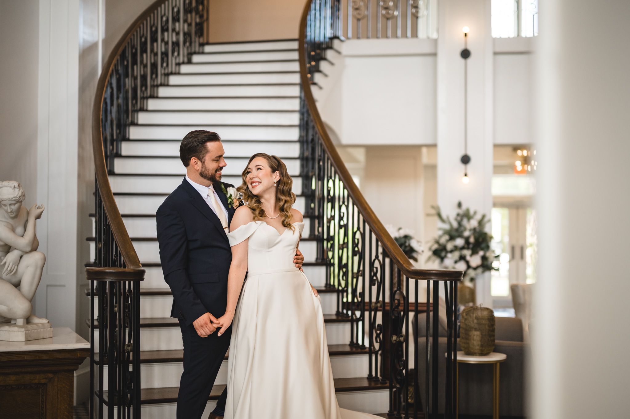 Elegant wedding first look sequence with couple by ornate staircase and white walls.