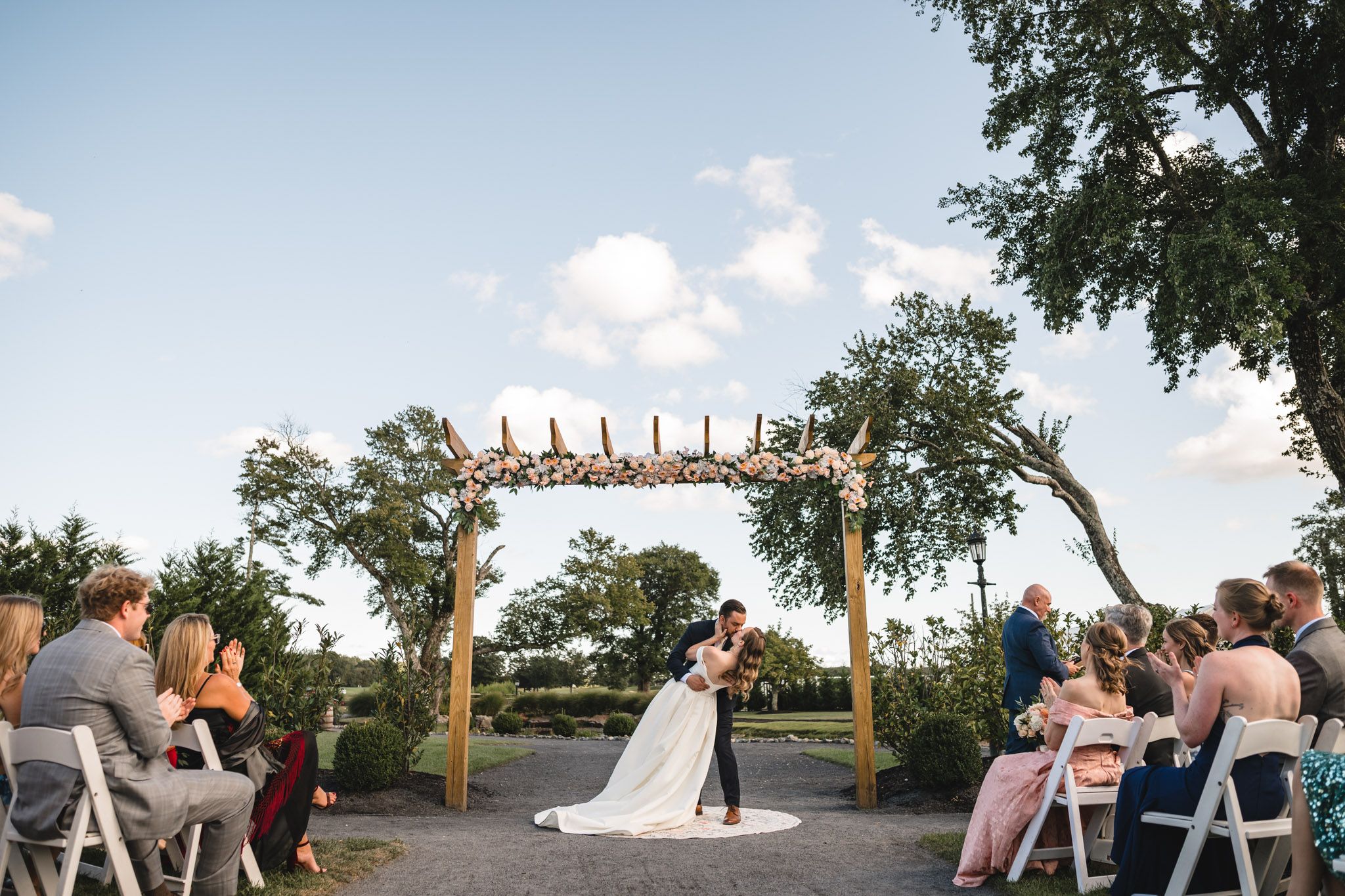 Panoramic view of an outdoor wedding ceremony space with wooden pergola and natural surroundings.