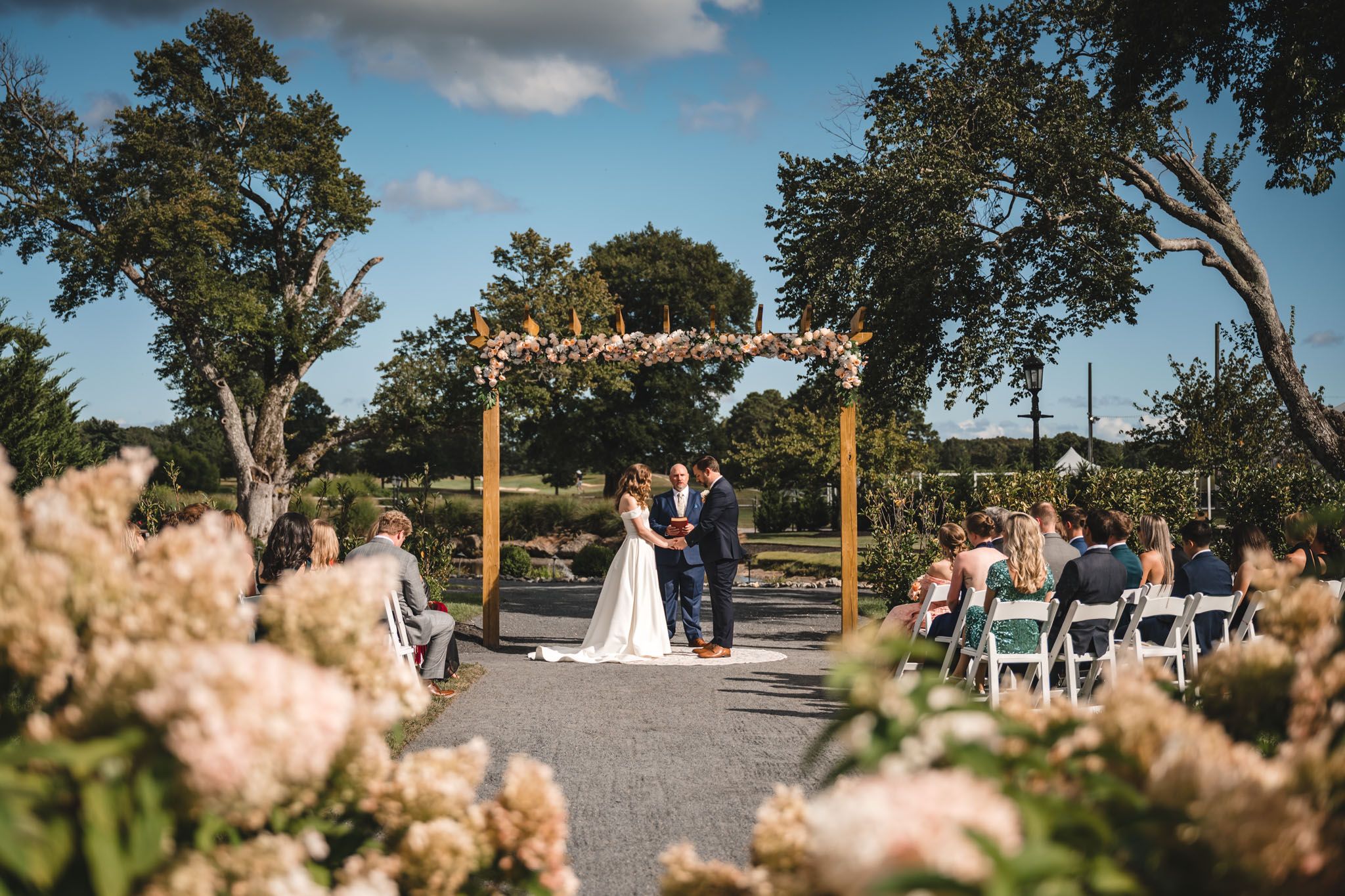 Outdoor wedding ceremony setup with rows of white chairs under blue skies.