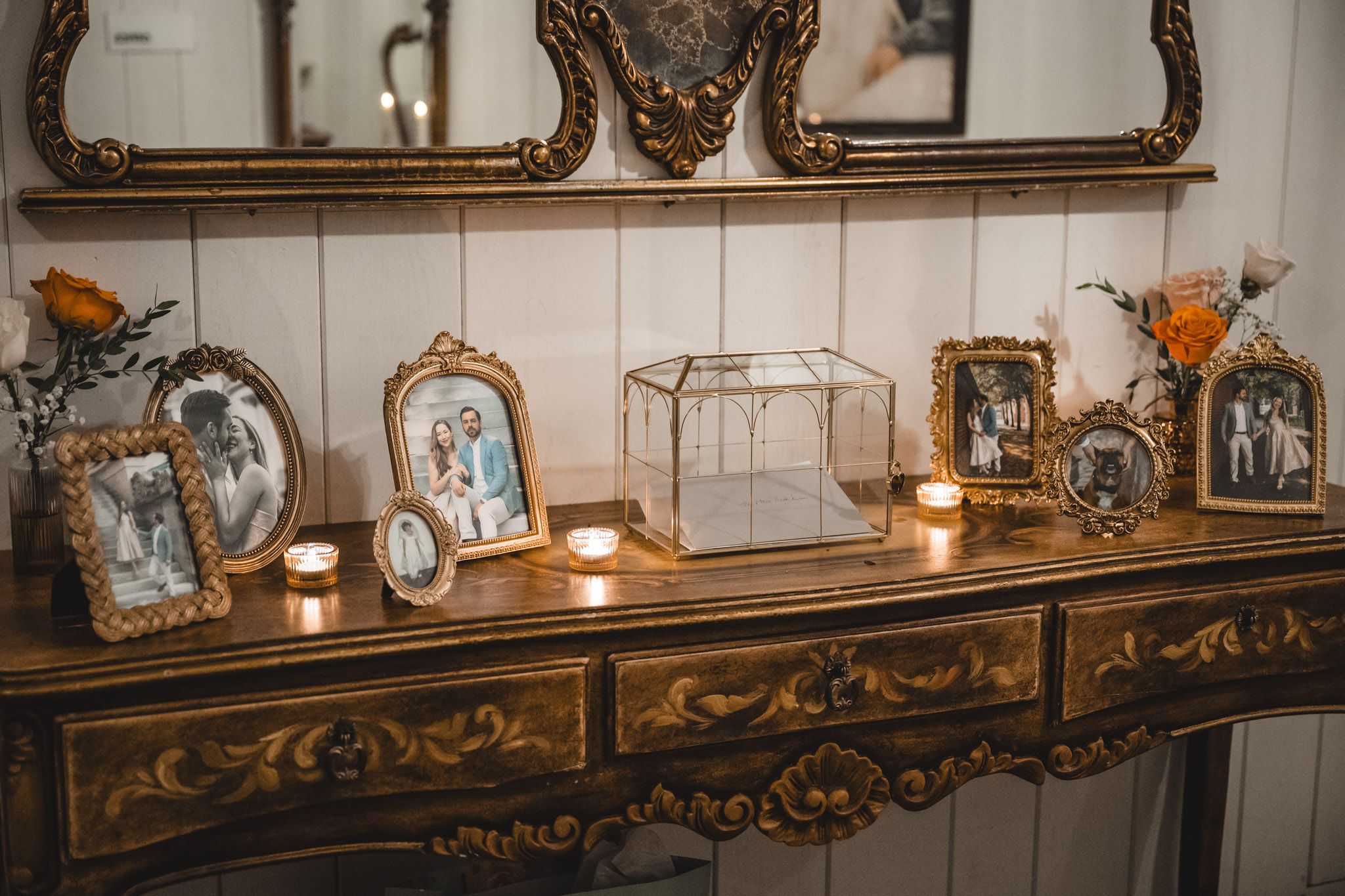 Ornate gold-framed mirrors and vintage decor adorn a white wall with candlelight.