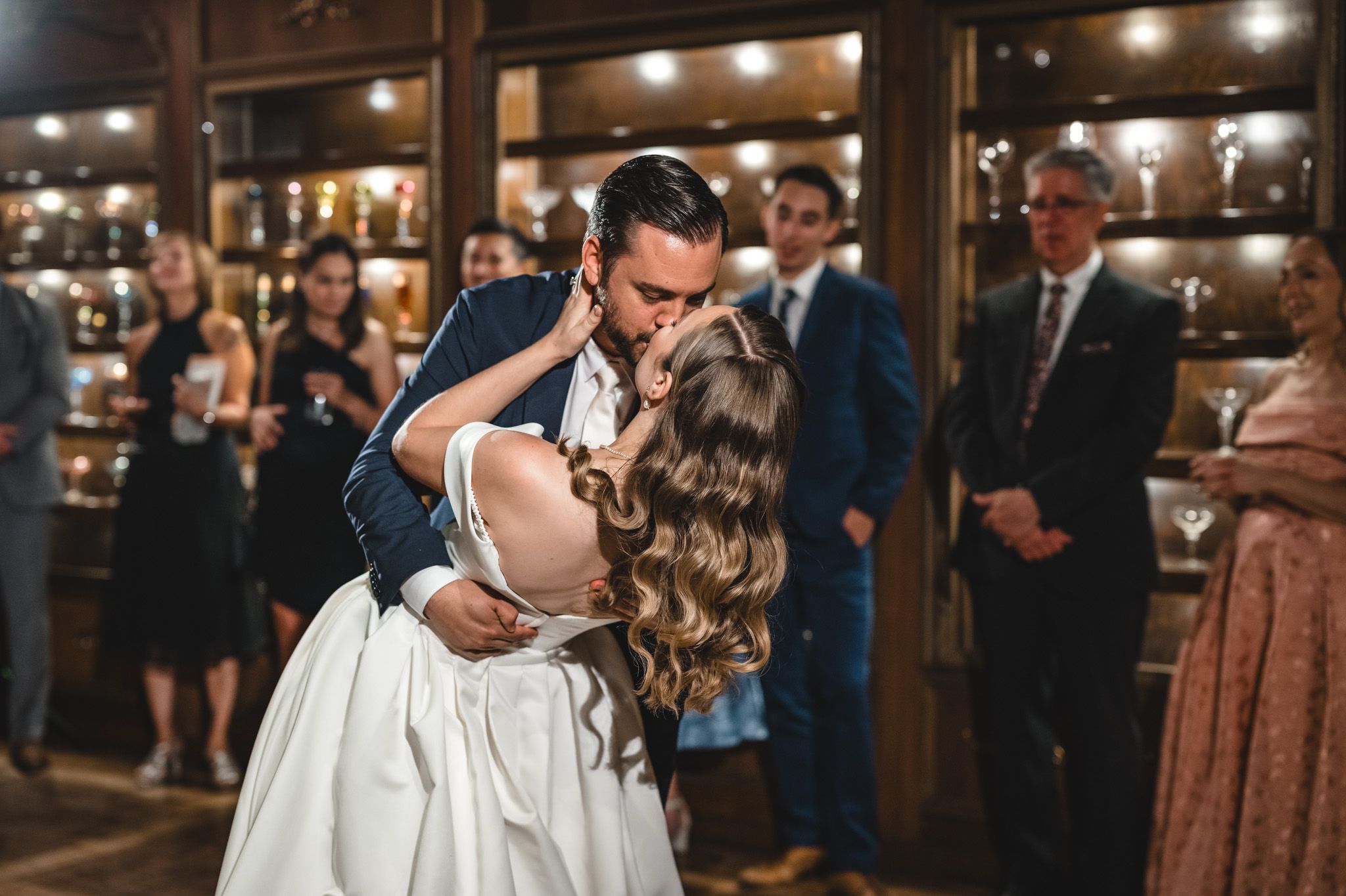 Wedding celebration in a warmly lit indoor venue with guests dancing and mingling on the dance floor.