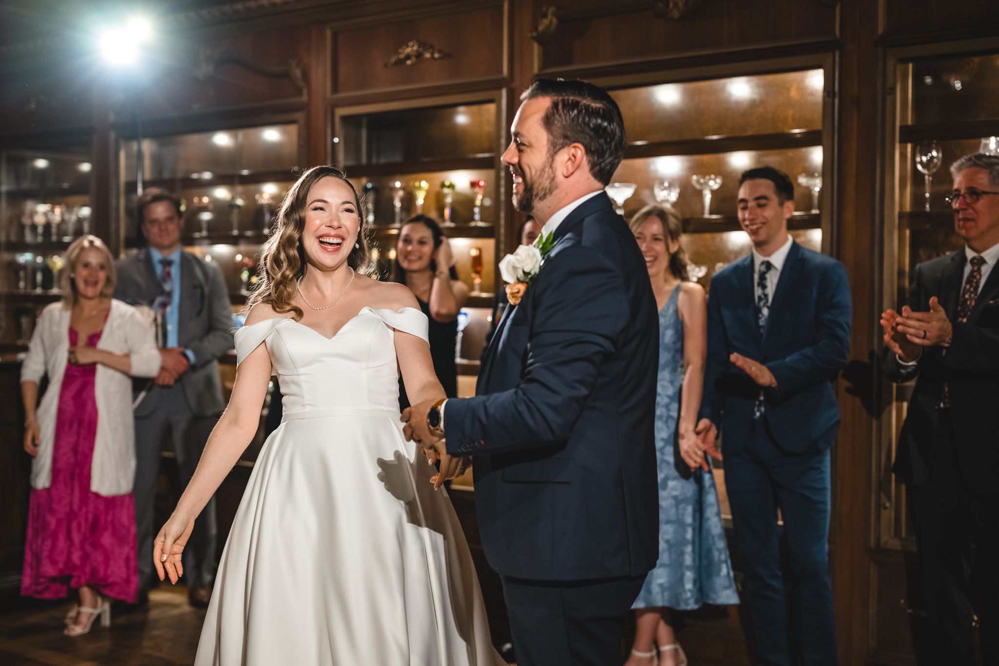 Wedding party celebrates with dancing and laughter in an atmospheric wood-paneled reception venue.