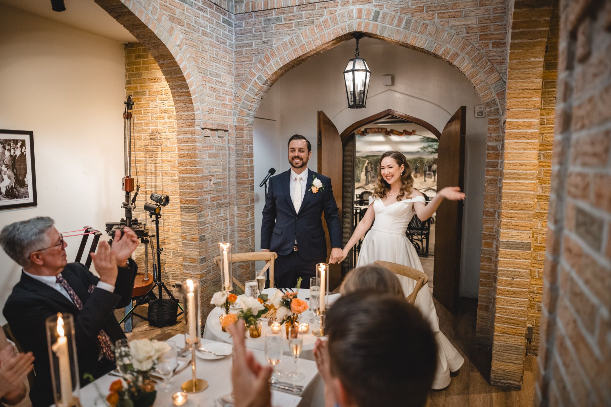 Wedding celebration in a rustic brick-walled venue with arched doorways and elegant lighting fixtures.