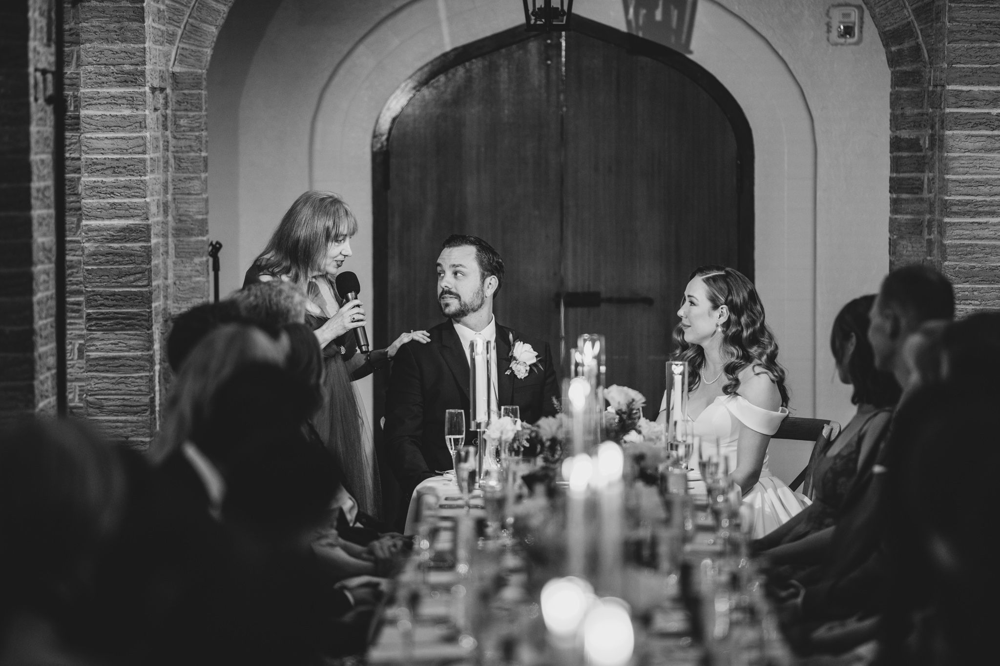Black and white photo of wedding guests celebrating in an elegant brick-walled reception space.
