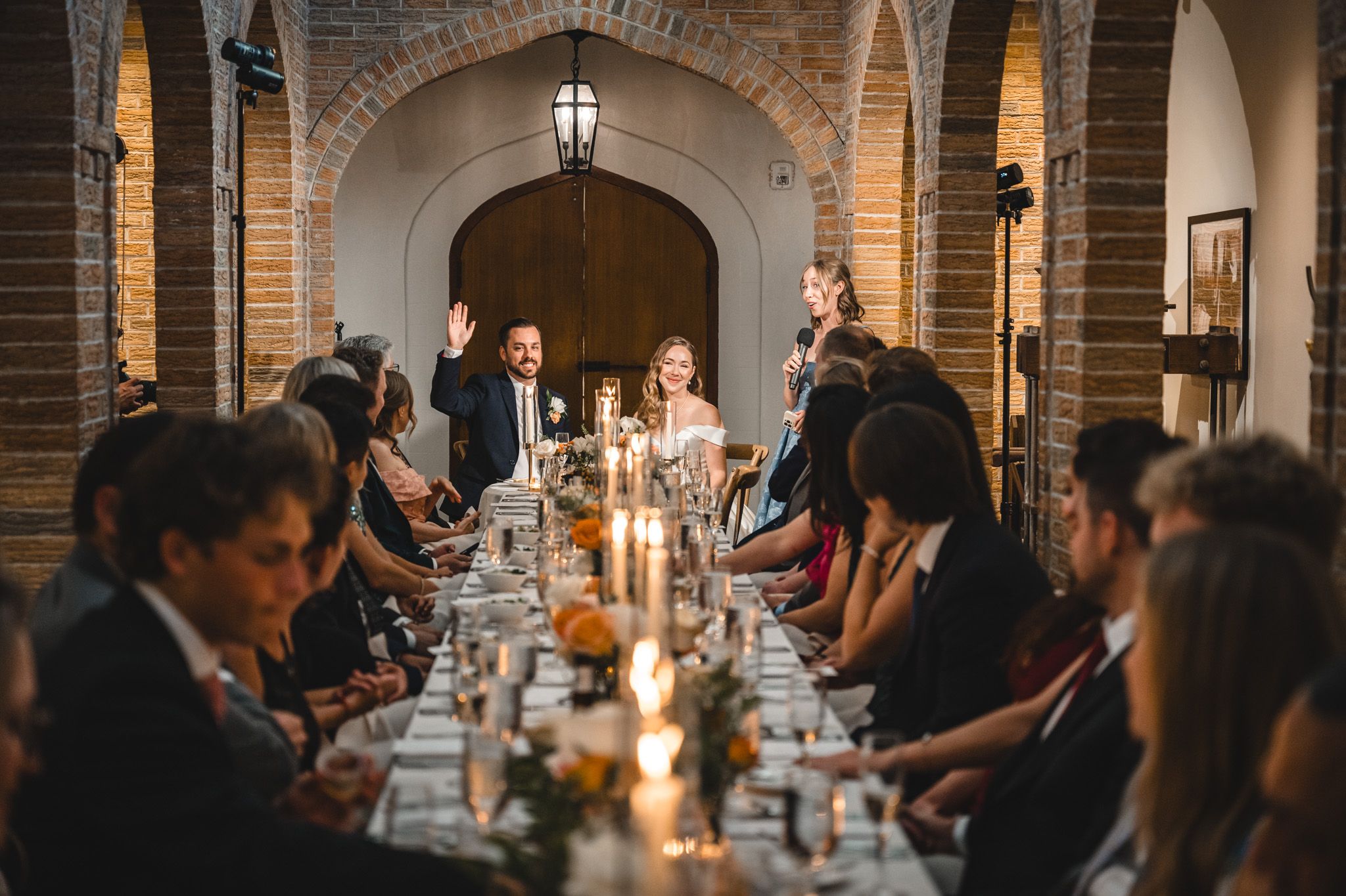 Elegant wedding reception dinner in a historic brick-arched venue with candlelit tables and guests dining.