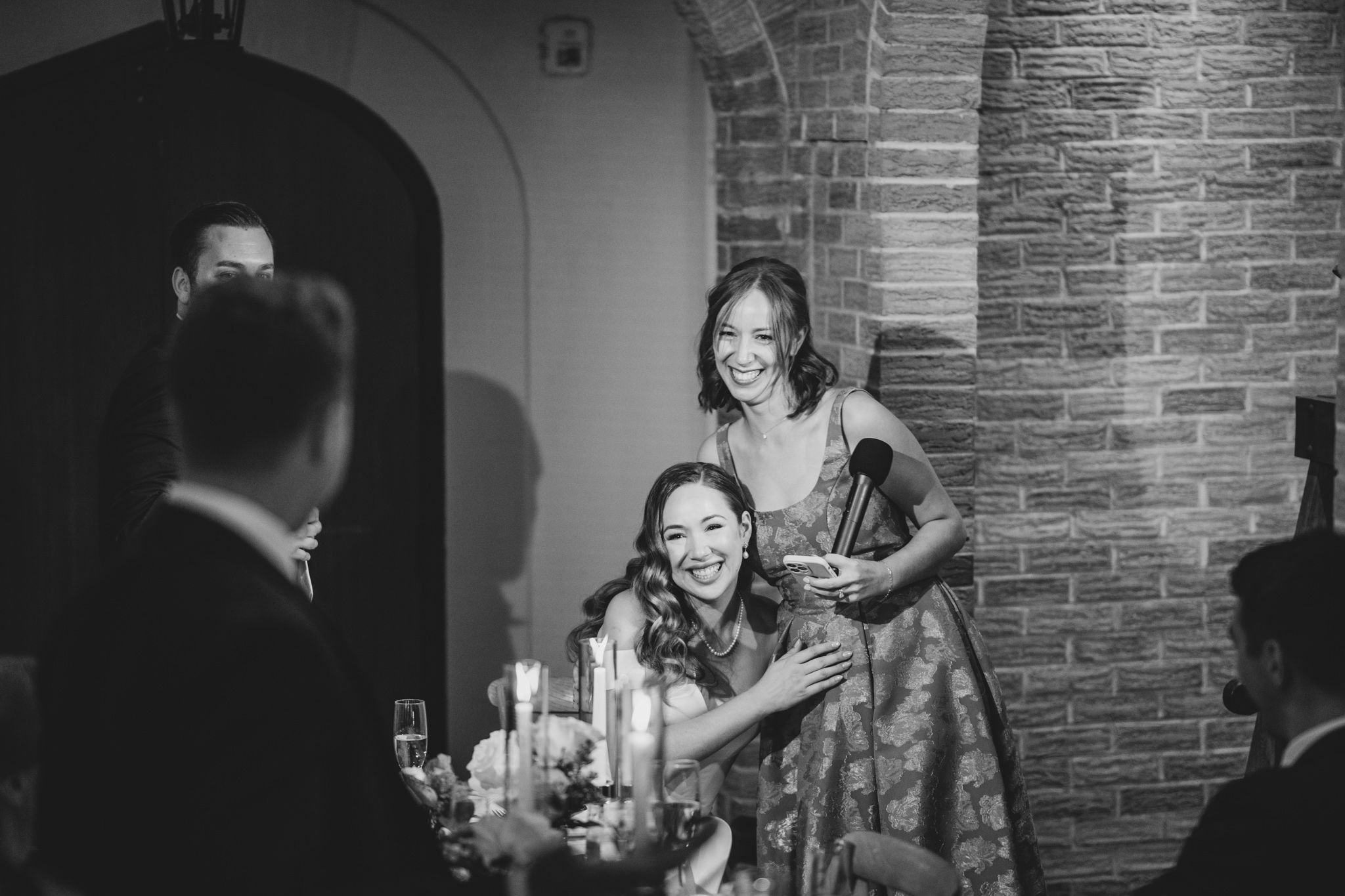 Intimate black and white reception scene with candlelit tables and brick walls creating ambiance.