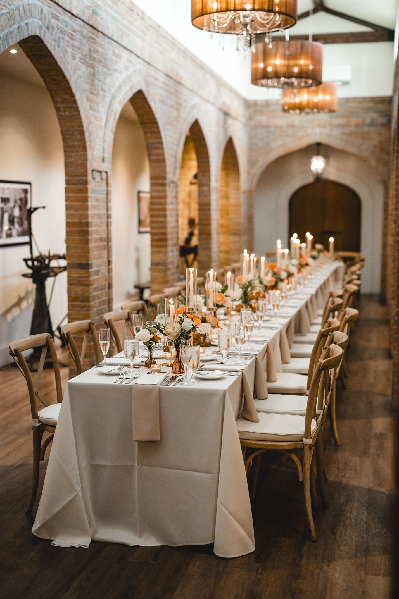 Elegant reception dining room with brick arches and long tables set with white linens and candles.