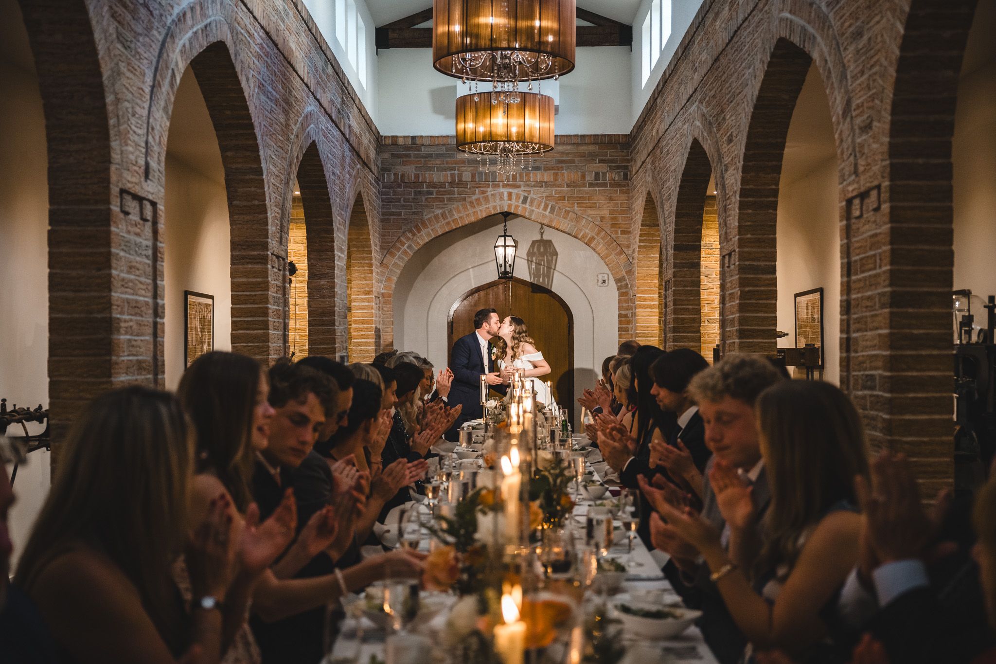Panoramic view of wedding reception dinner under dramatic arched ceilings with hanging chandeliers.