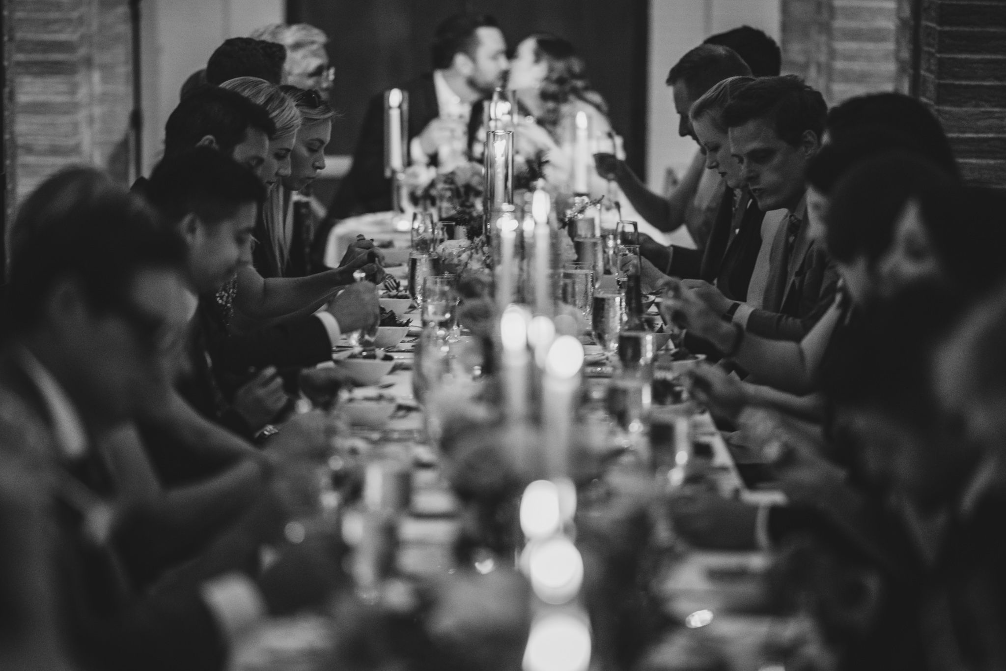 Black and white panorama of wedding guests dining at long tables with candlelight.