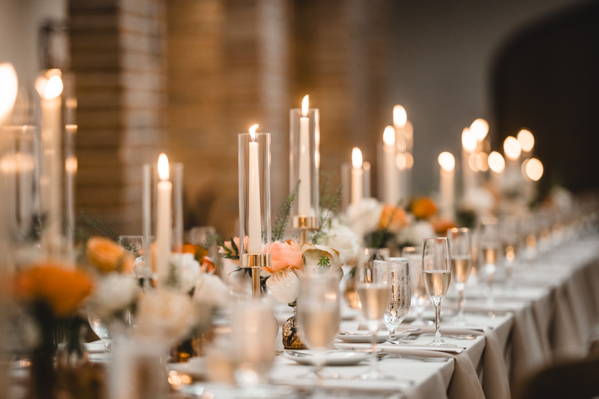 Candlelit wedding reception tables with elegant place settings and warm ambient lighting.