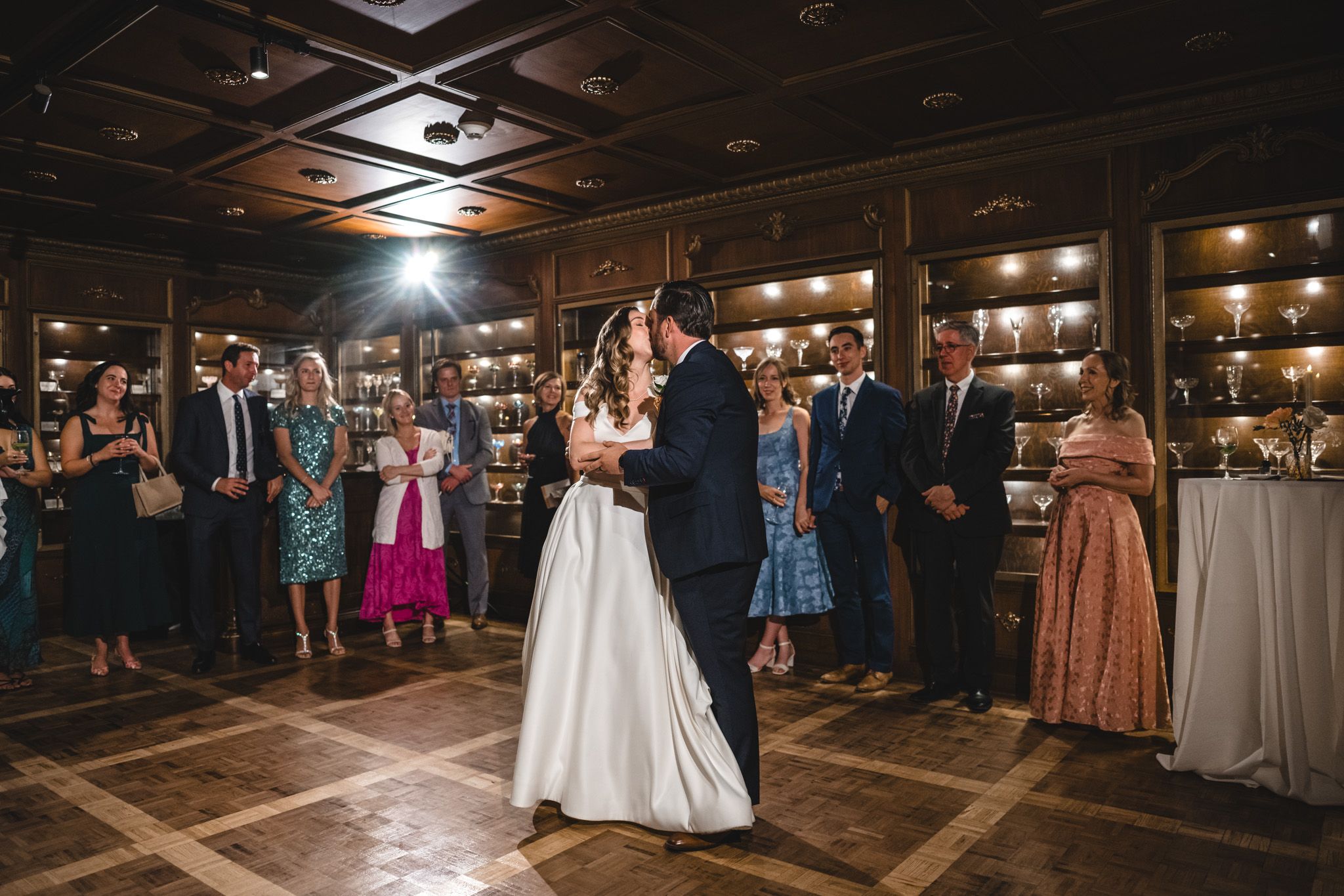 Guests gather around a dance floor at an elegant indoor wedding reception with wood beam ceiling details.