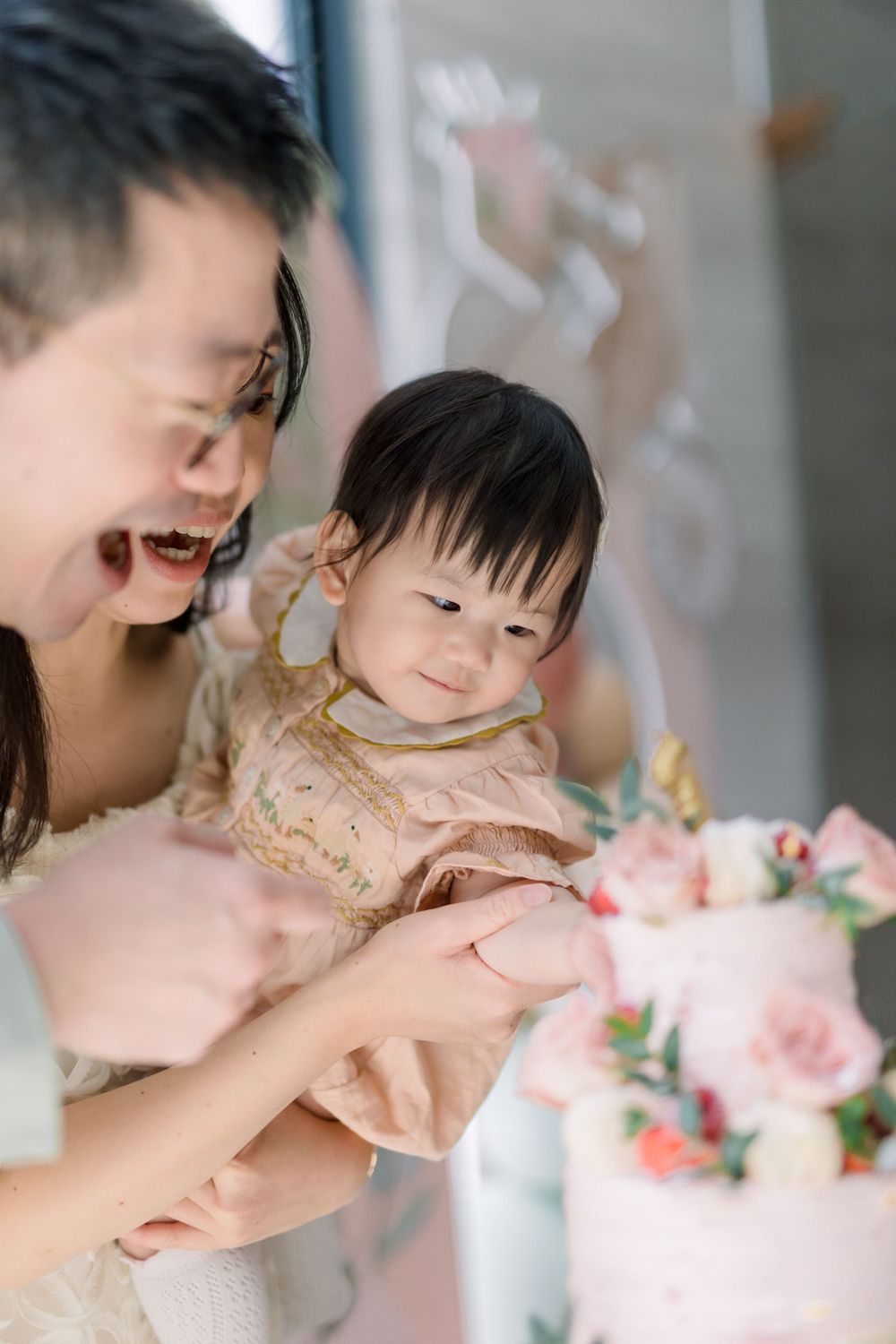 A birthday celebration shows a child wearing pink reaching towards a decorated cake in a soft, dreamy atmosphere.