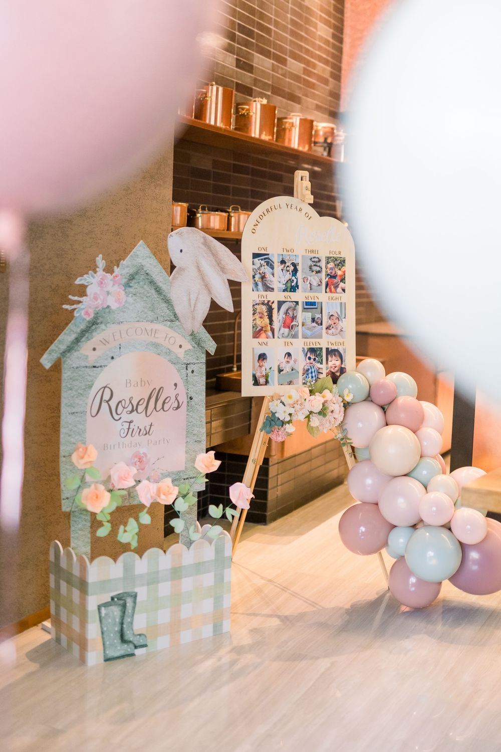 Baby shower decor featuring mint green and pink balloon arch, gingham backdrop, and photo display at a party venue.