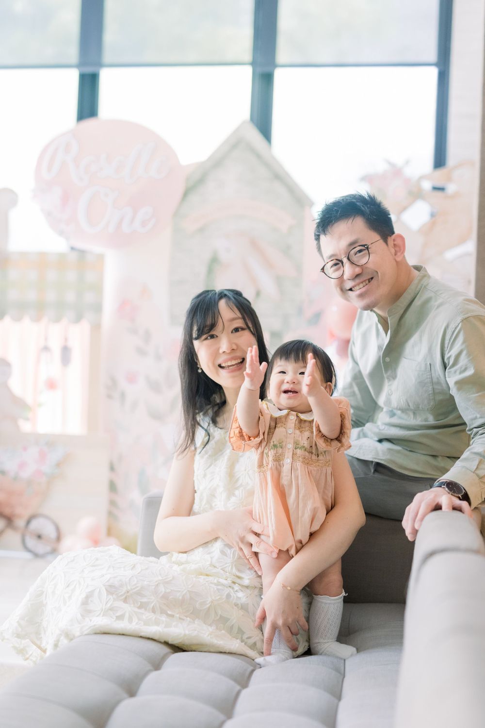 A family sitting on a couch in a bright room with pink decorations and white accents.