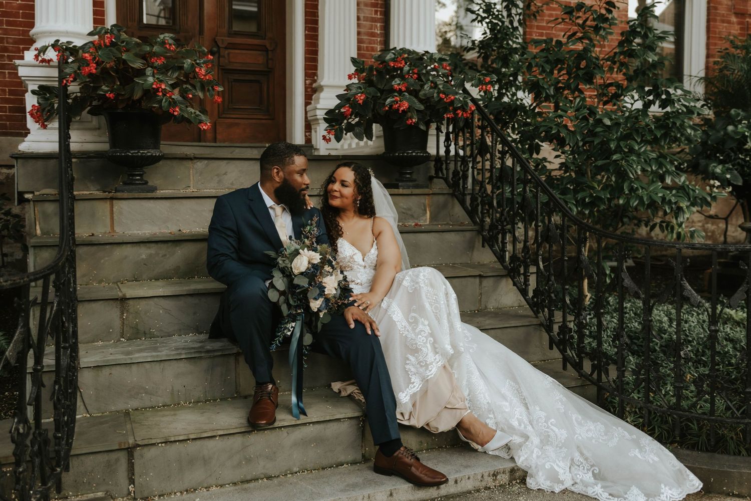 Wedding couple sitting on brick steps with floral bouquet and lace dress.