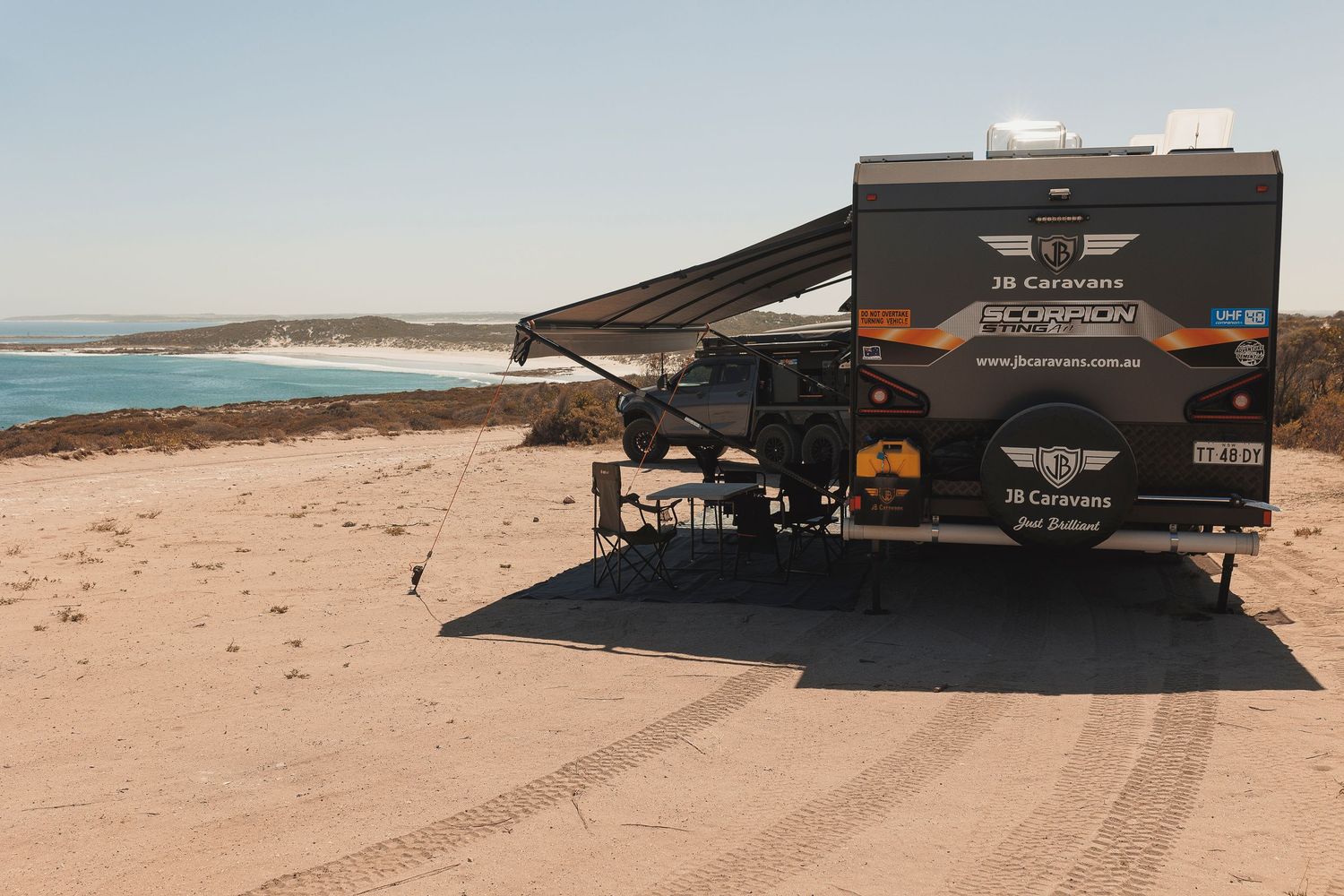 A black recreational vehicle drives along a sandy beach with ocean waves visible in the distance.