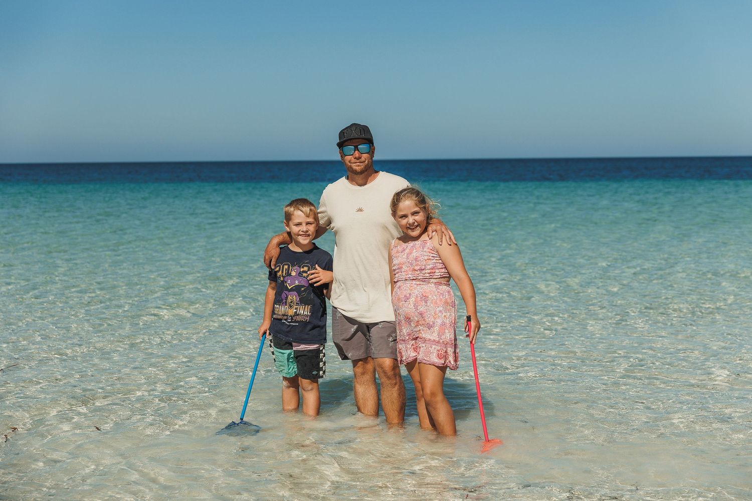 Family wading in crystal clear turquoise water at tropical beach during summer vacation.