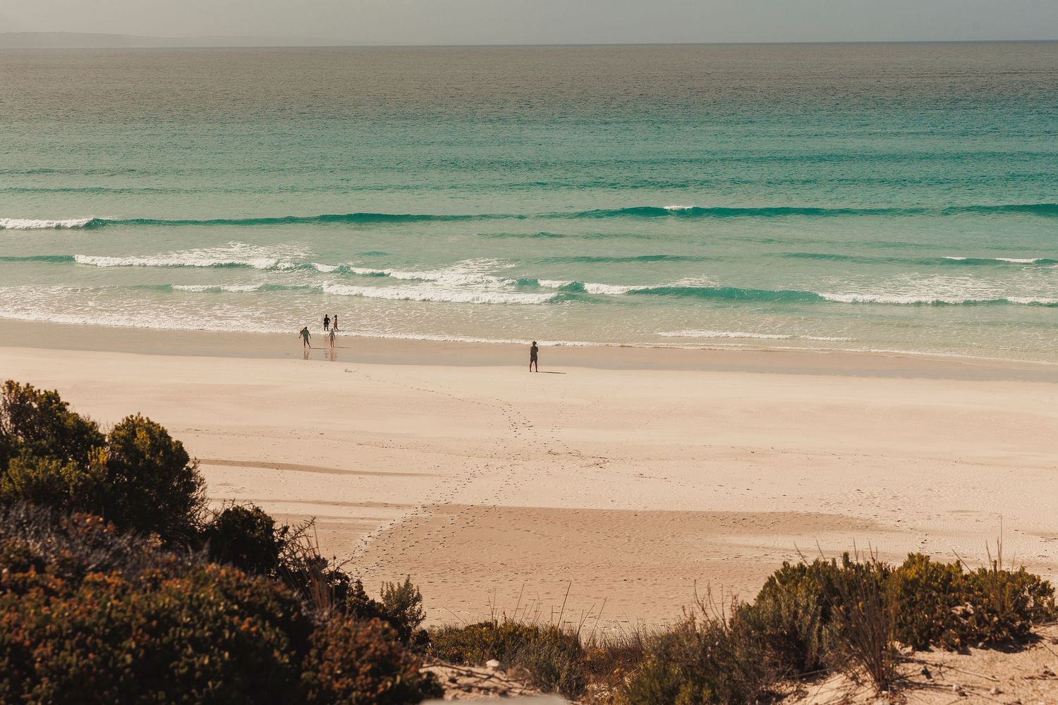 Panoramic view of a beautiful turquoise ocean coastline with white sandy beach and people walking along the shore.