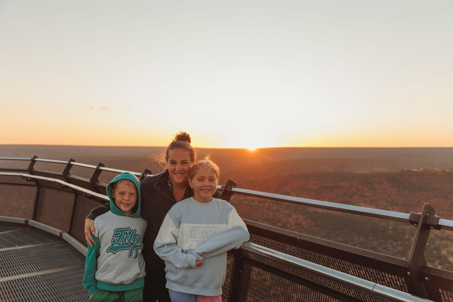 A group enjoying sunset views from a wooden observation deck surrounded by rolling hills during golden hour.