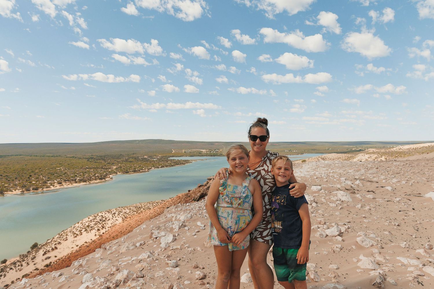 A scenic coastal road curves along a turquoise lake surrounded by desert landscape on a sunny day.