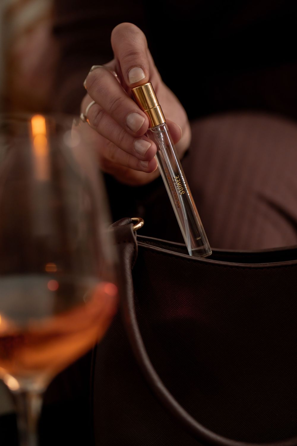 Hands holding elegant glassware in a dimly lit bar setting with amber-colored drinks.