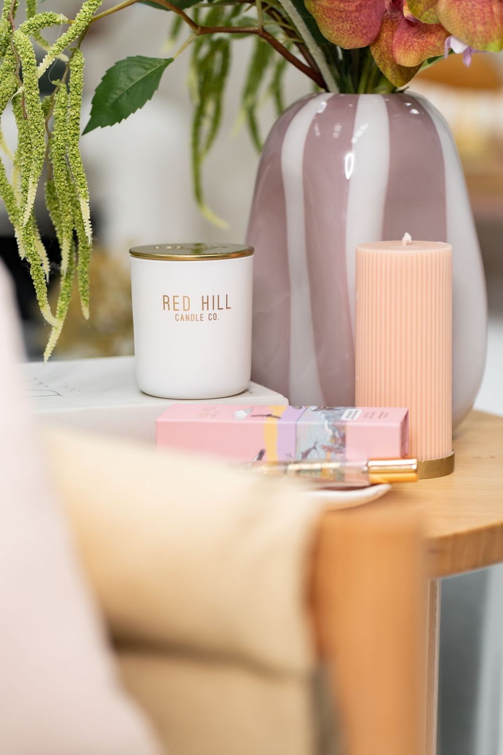 Soft pink decor items including candles and vases arranged on a wooden shelf with green foliage accents.