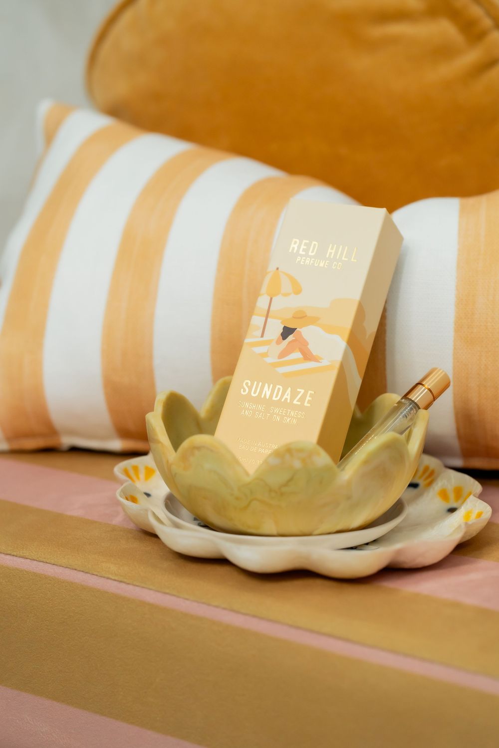 Red Hill book titled 'Sundaze' displayed in a golden lotus-shaped dish on striped cushions.